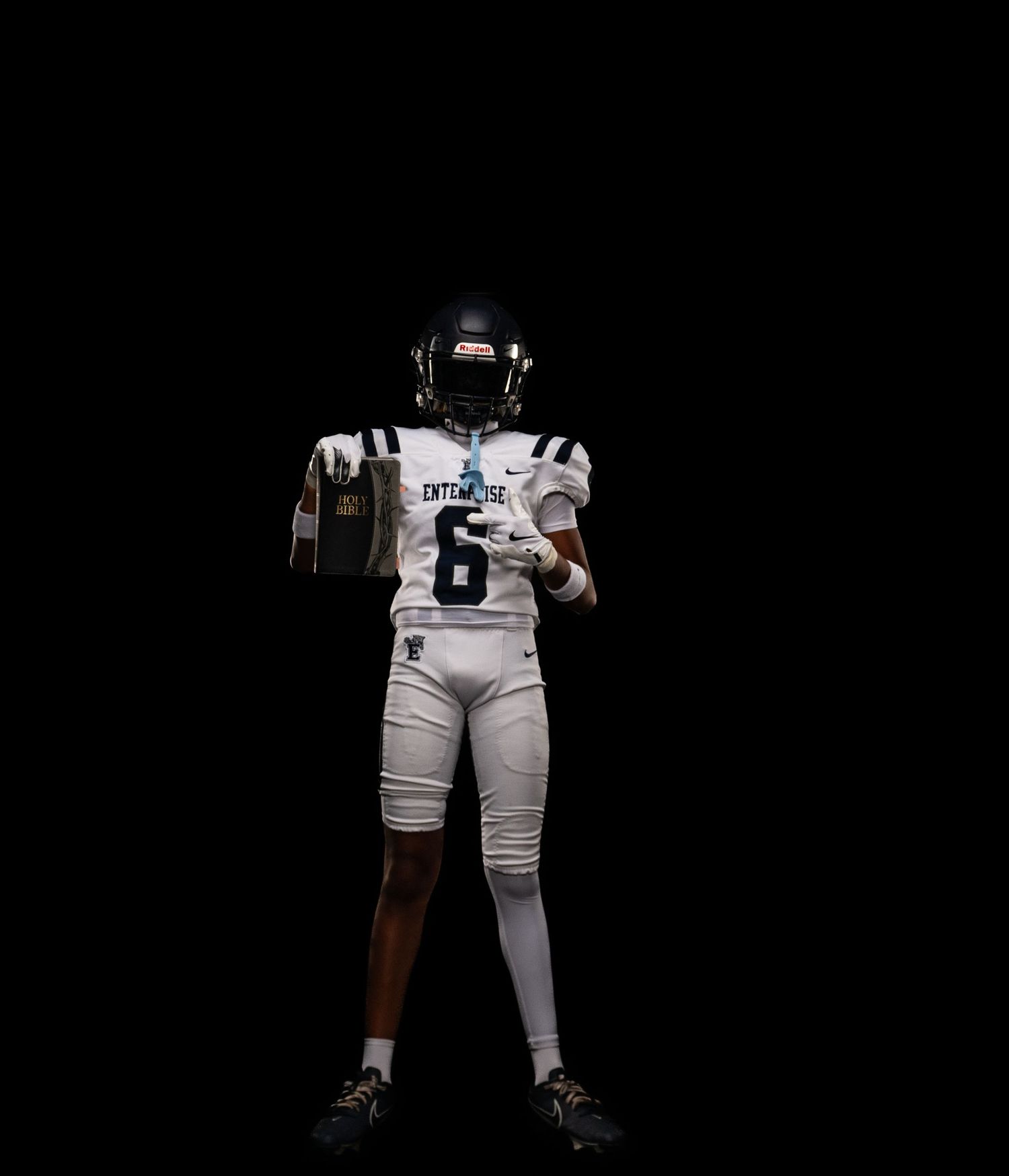 Football player in white Enterprise #6 jersey and helmet holds trophy against black background.