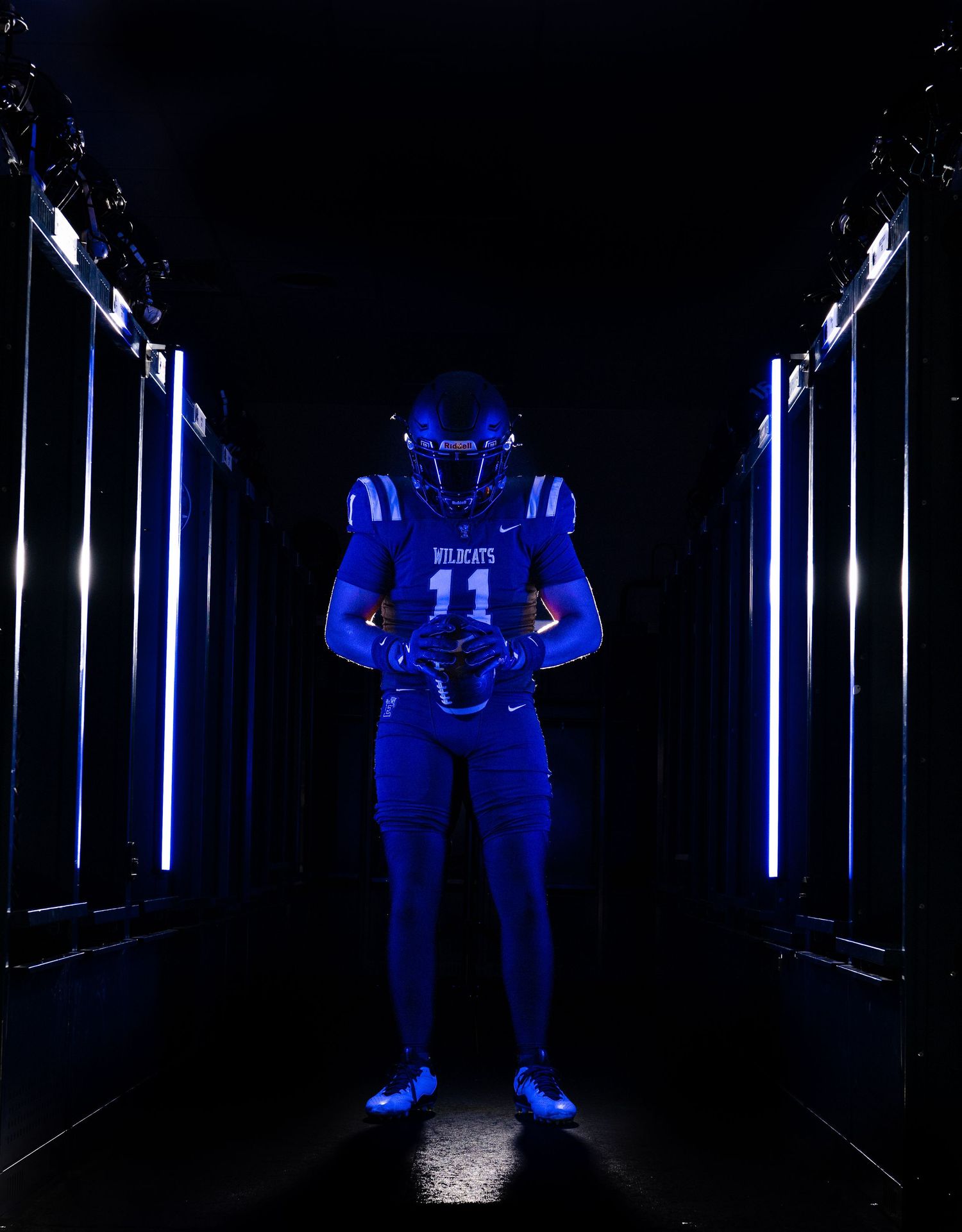 Wildcats #11 football player in blue uniform posed in dramatic dark tunnel with neon lights.