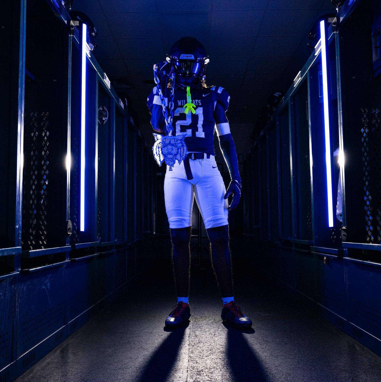 Football player number 21 in blue uniform stands in dramatically lit tunnel with glowing blue lights.