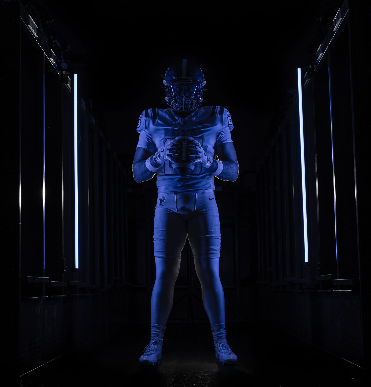 Football player in blue uniform poses dramatically in dark tunnel with glowing LED light strips.