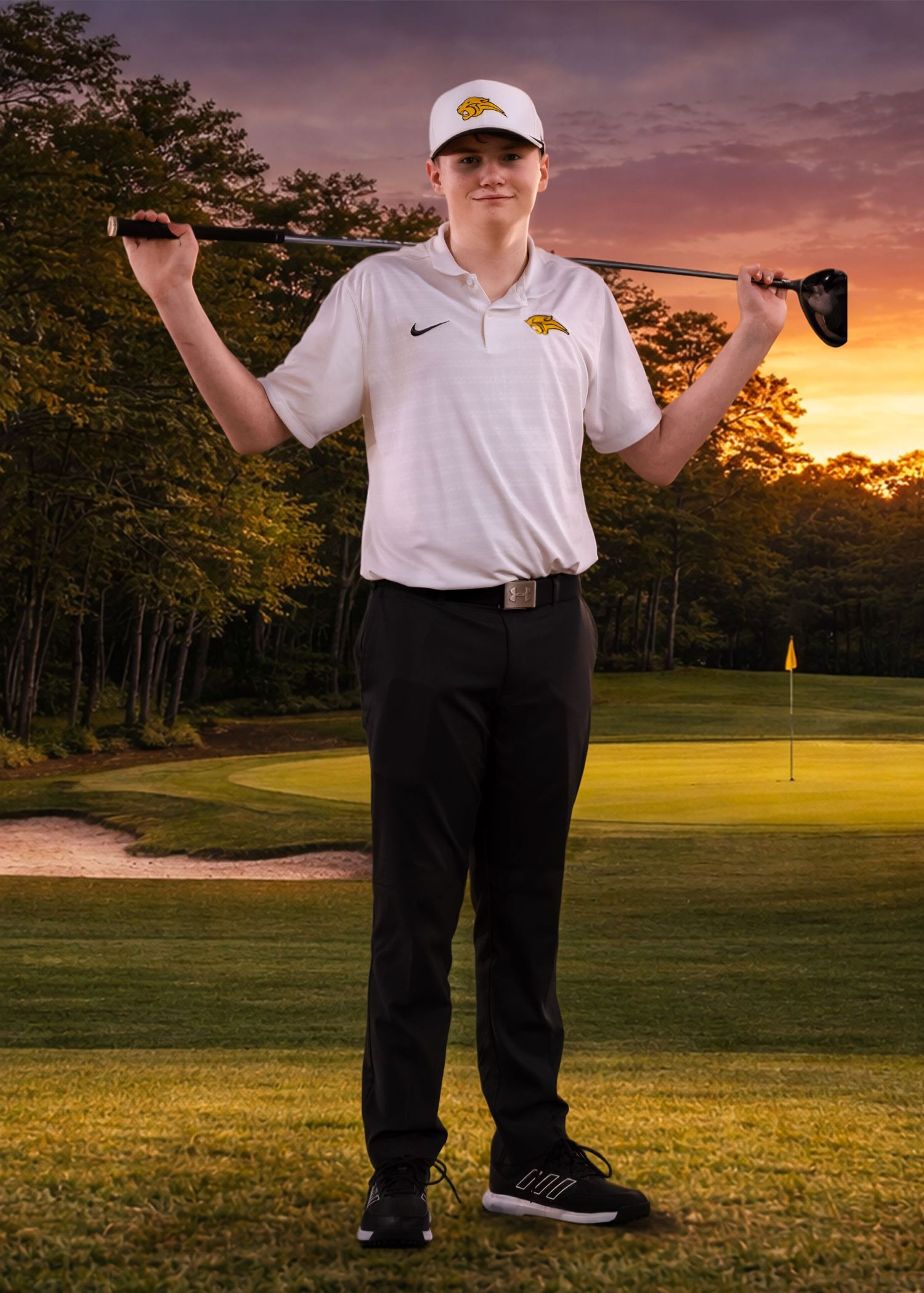 Golfer in white polo and black pants posing with golf club on lush course at golden hour.