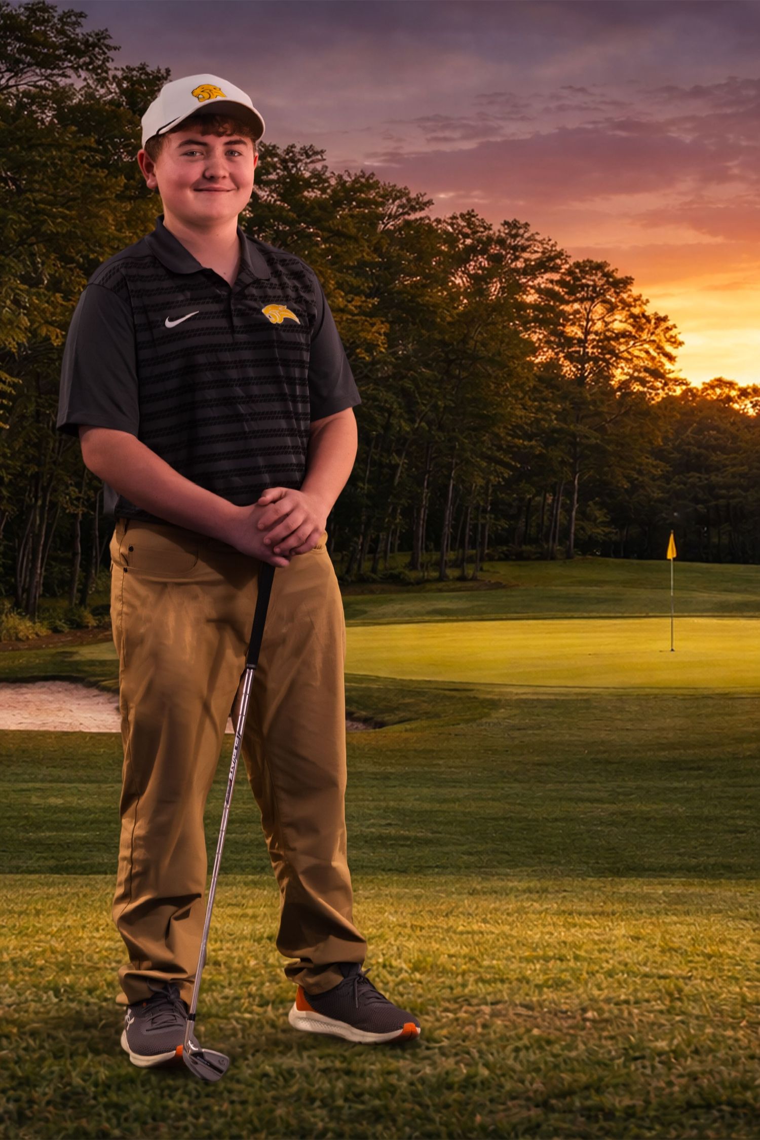 A golfer stands on a lush green course during a vibrant sunset with trees silhouetted in the background.