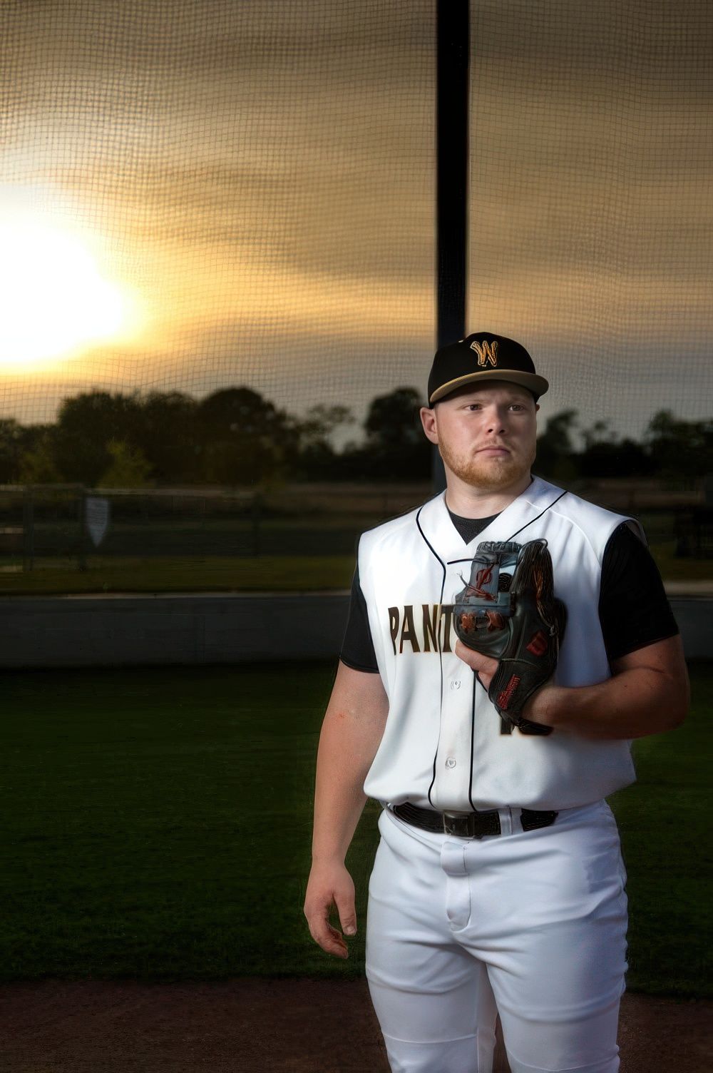 Baseball player in white Panther uniform poses at sunset with glove and ball.