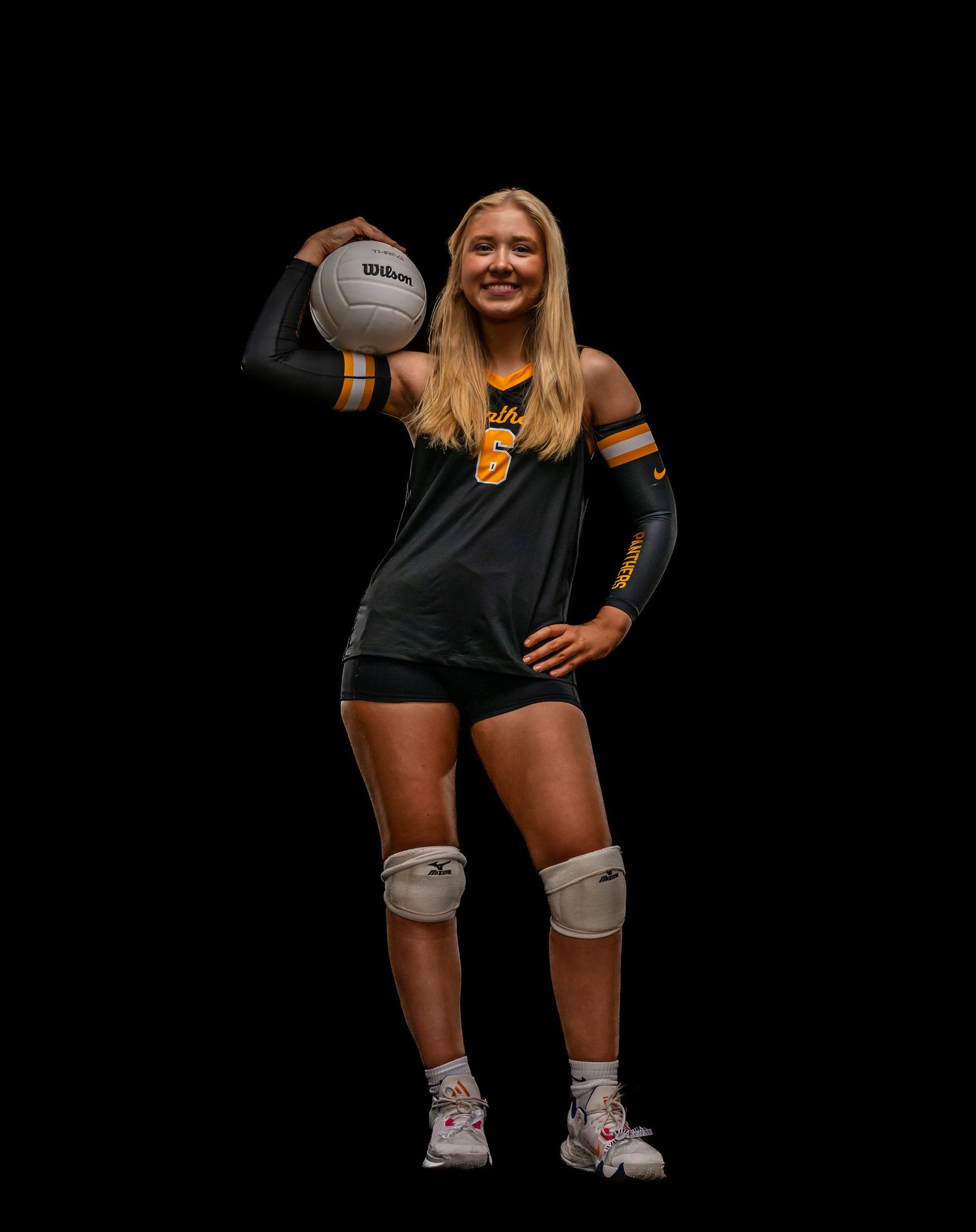 Volleyball players in dark uniforms crouch in defensive positions with knee pads.