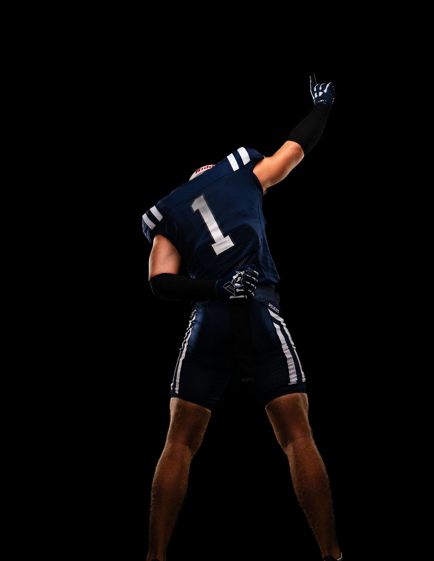 Football player in navy jersey with number 1 poses against black background.