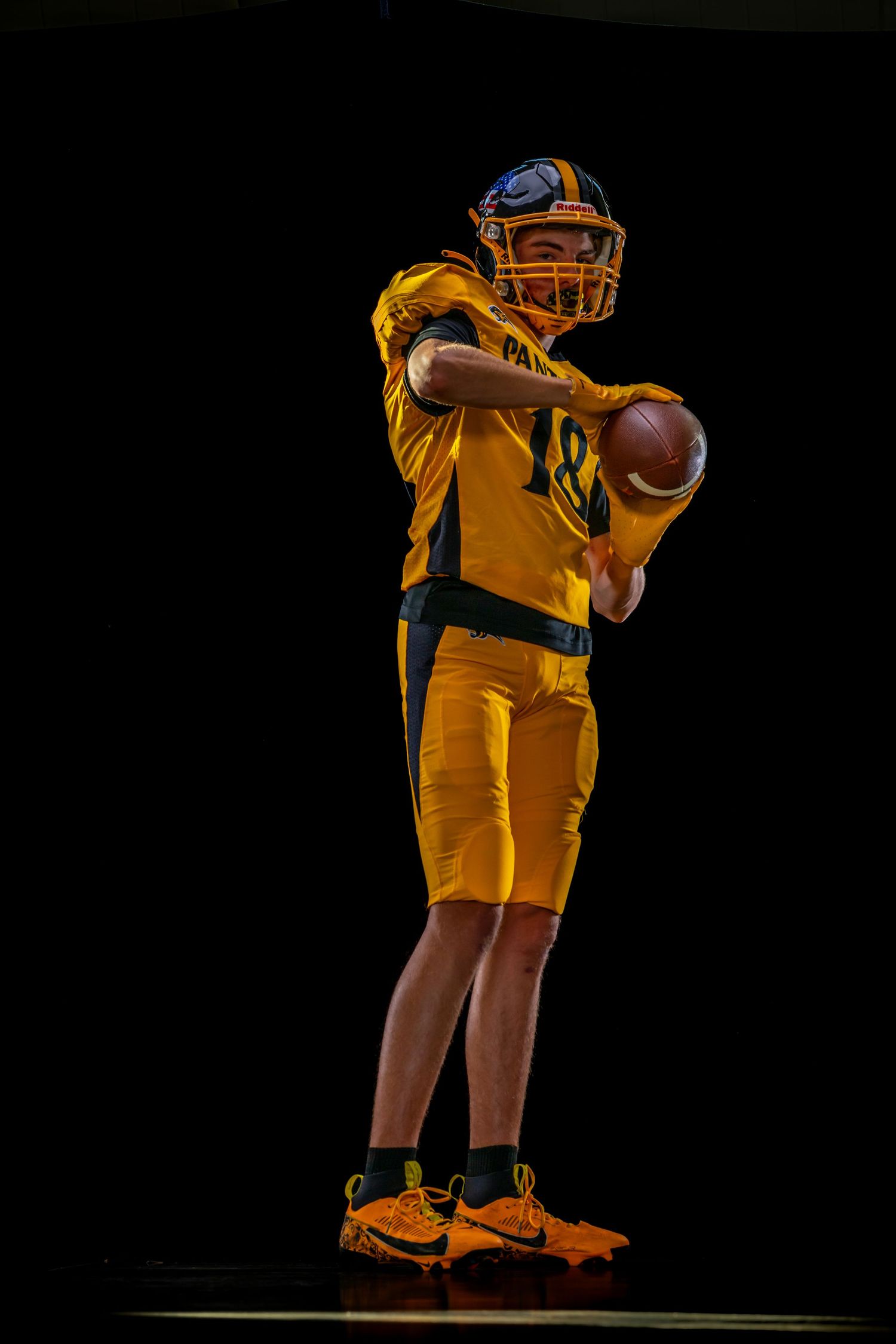 American football player in yellow uniform holding ball, poised to throw against dark background.