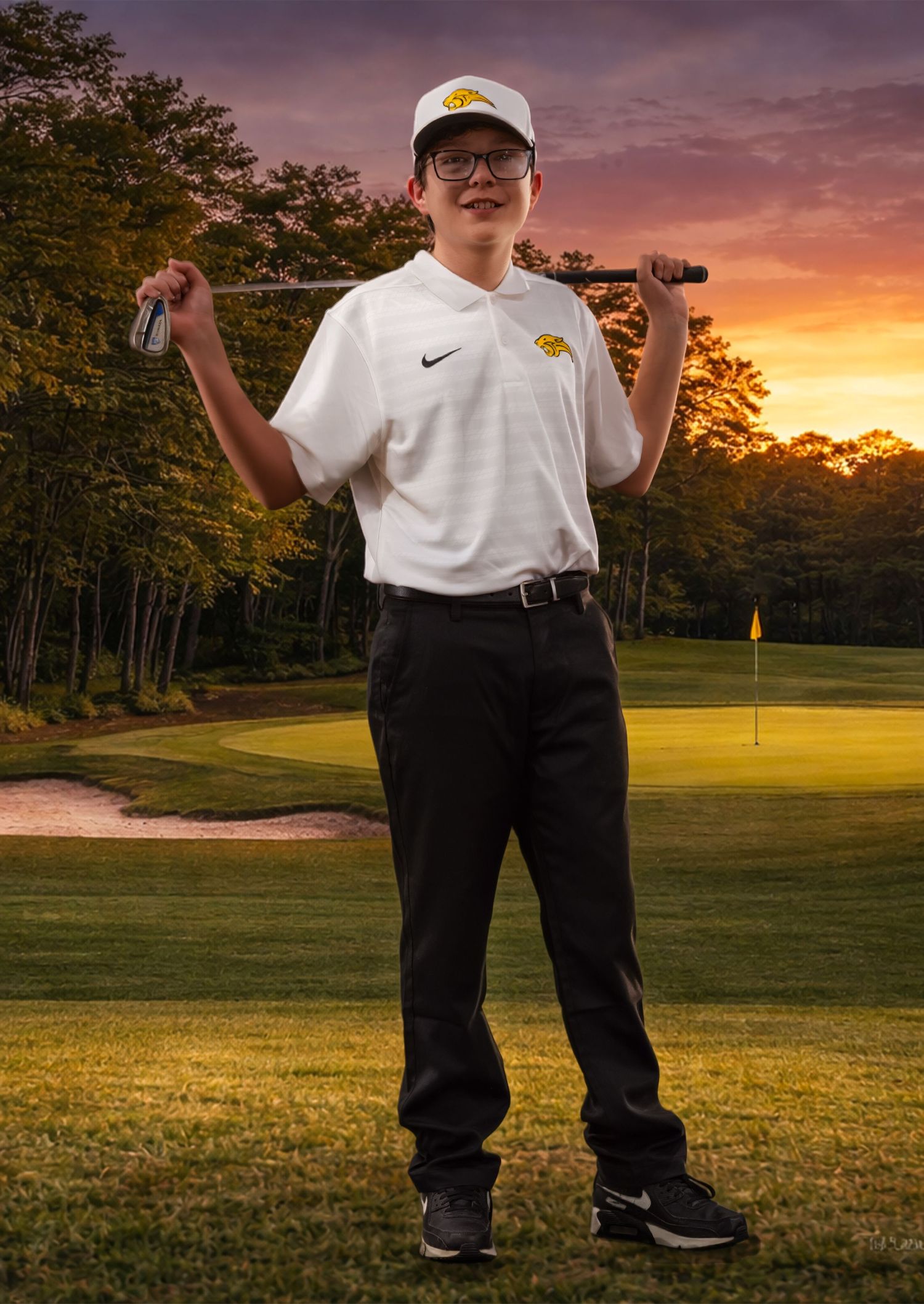 Golfer stands on lush green course at sunset with vibrant orange sky and trees in background.