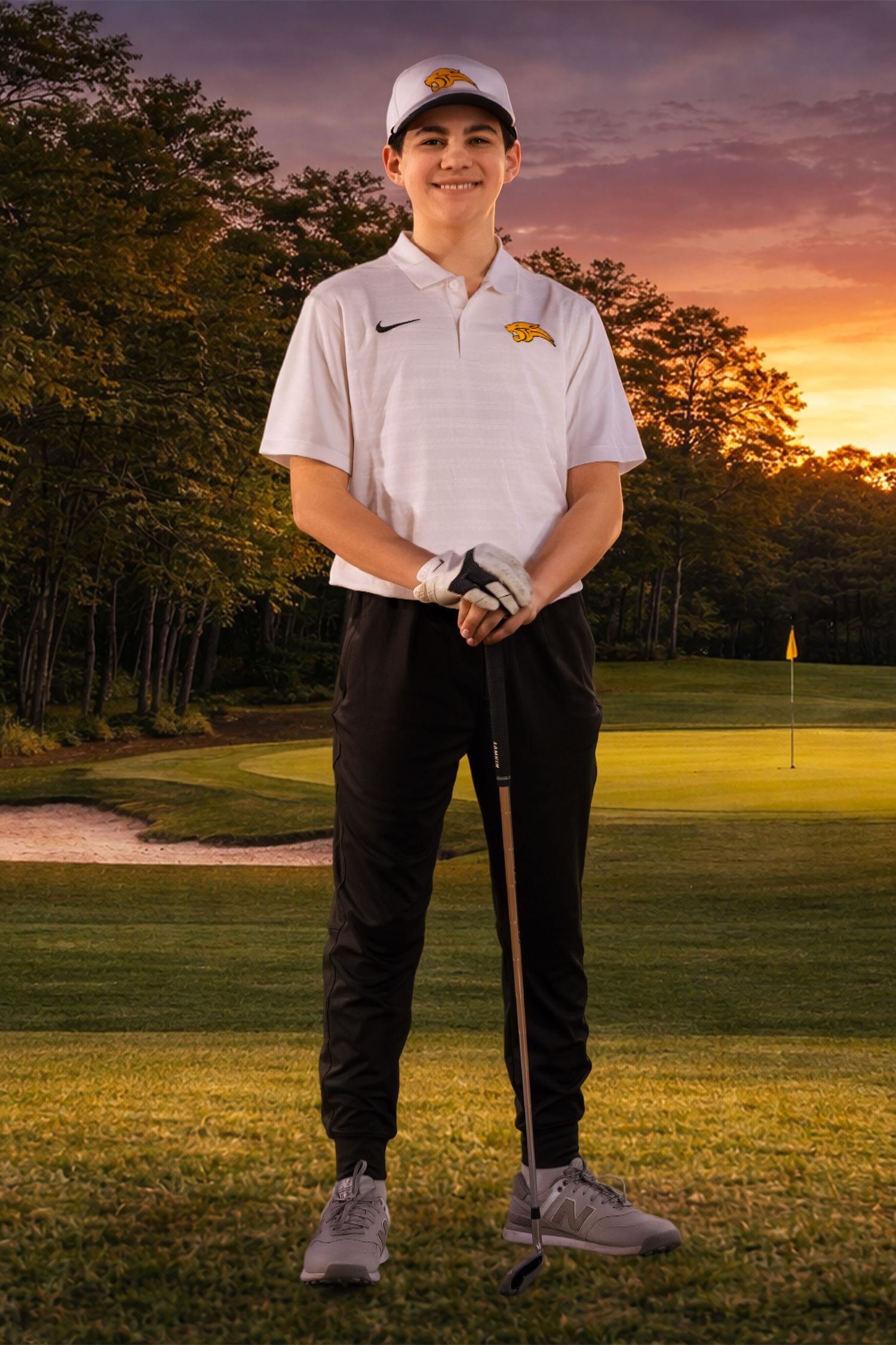 Golfer in white polo and black pants poses with club on scenic course at dusk.