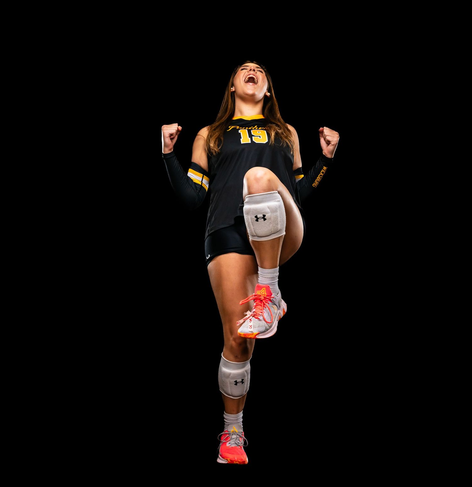 Volleyball player demonstrates jumping technique in black uniform against dark backdrop.