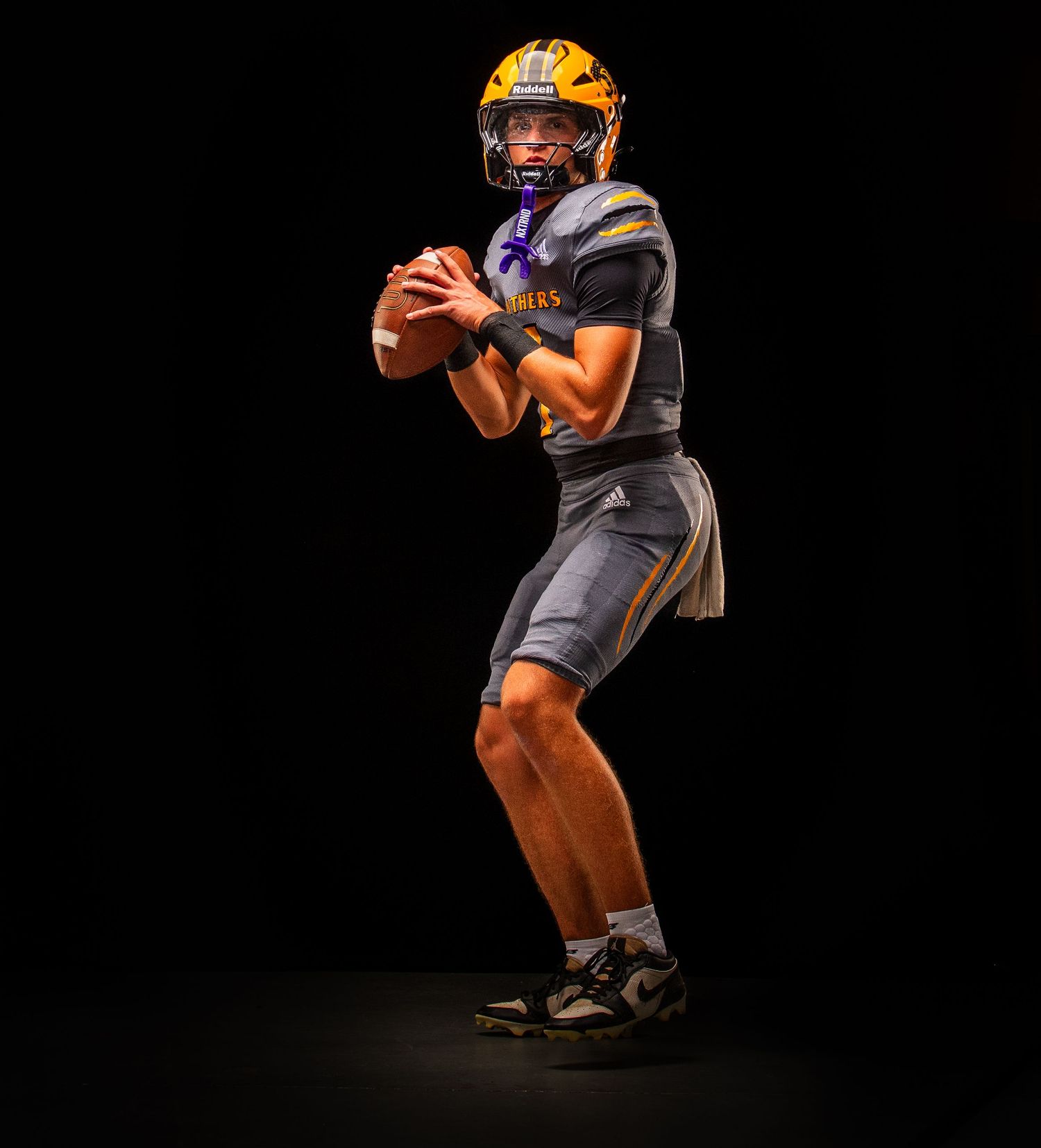 Football player in orange and gray uniform demonstrating offensive stance on dark background.