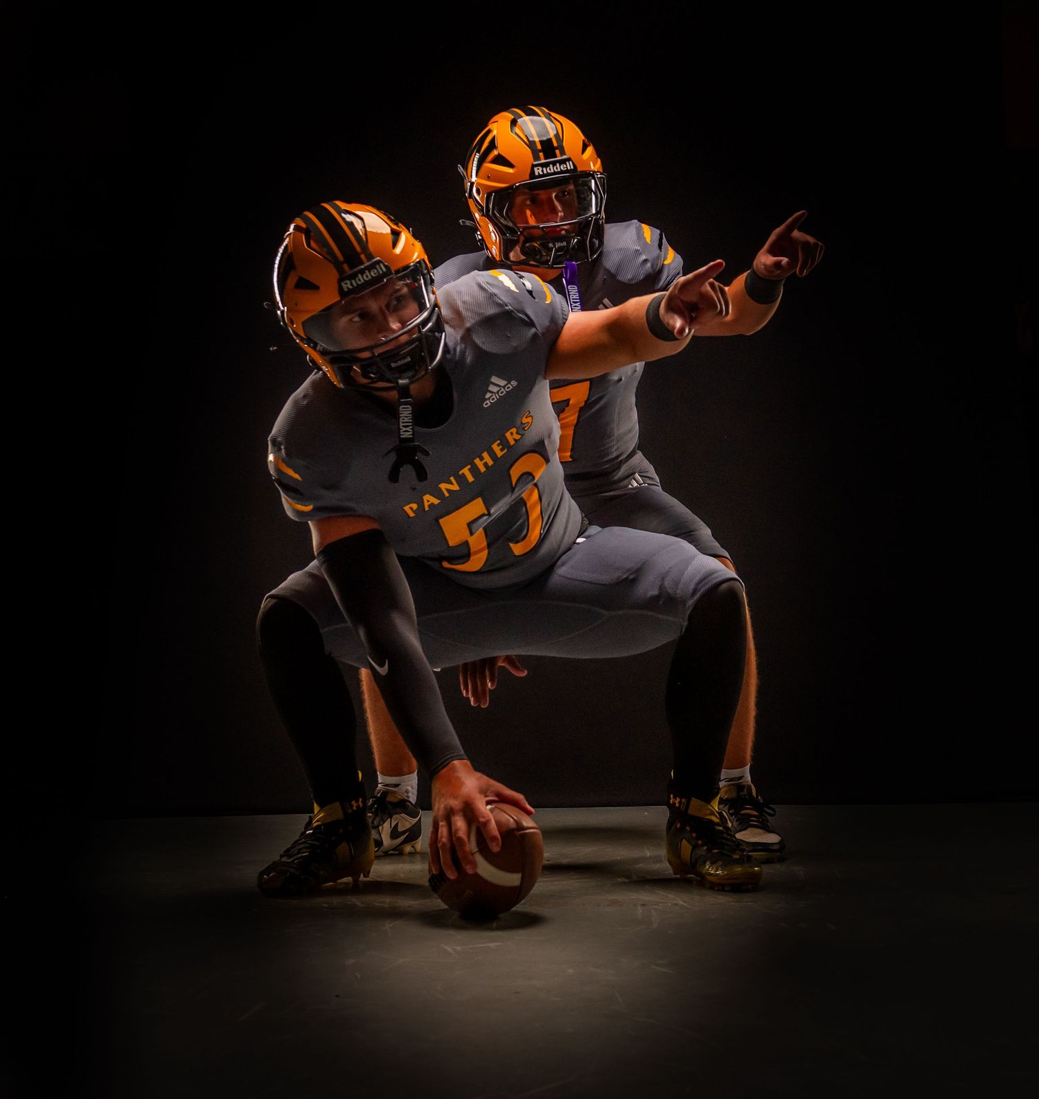 Two football players in orange and gray Panthers uniforms pose dynamically on a dark studio background.