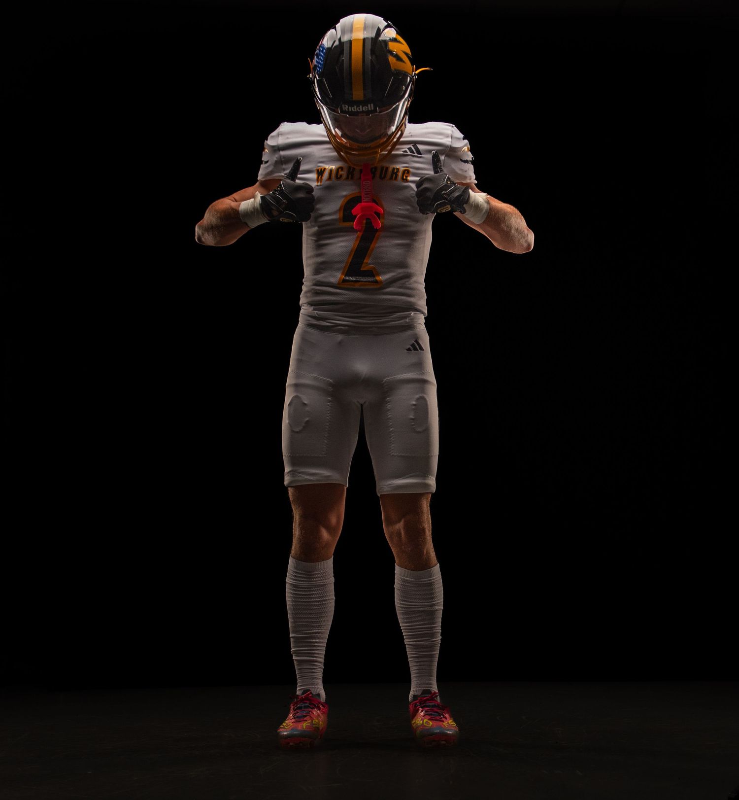 Football player in gray uniform and gold helmet poses against dark background, wearing number 2 jersey.