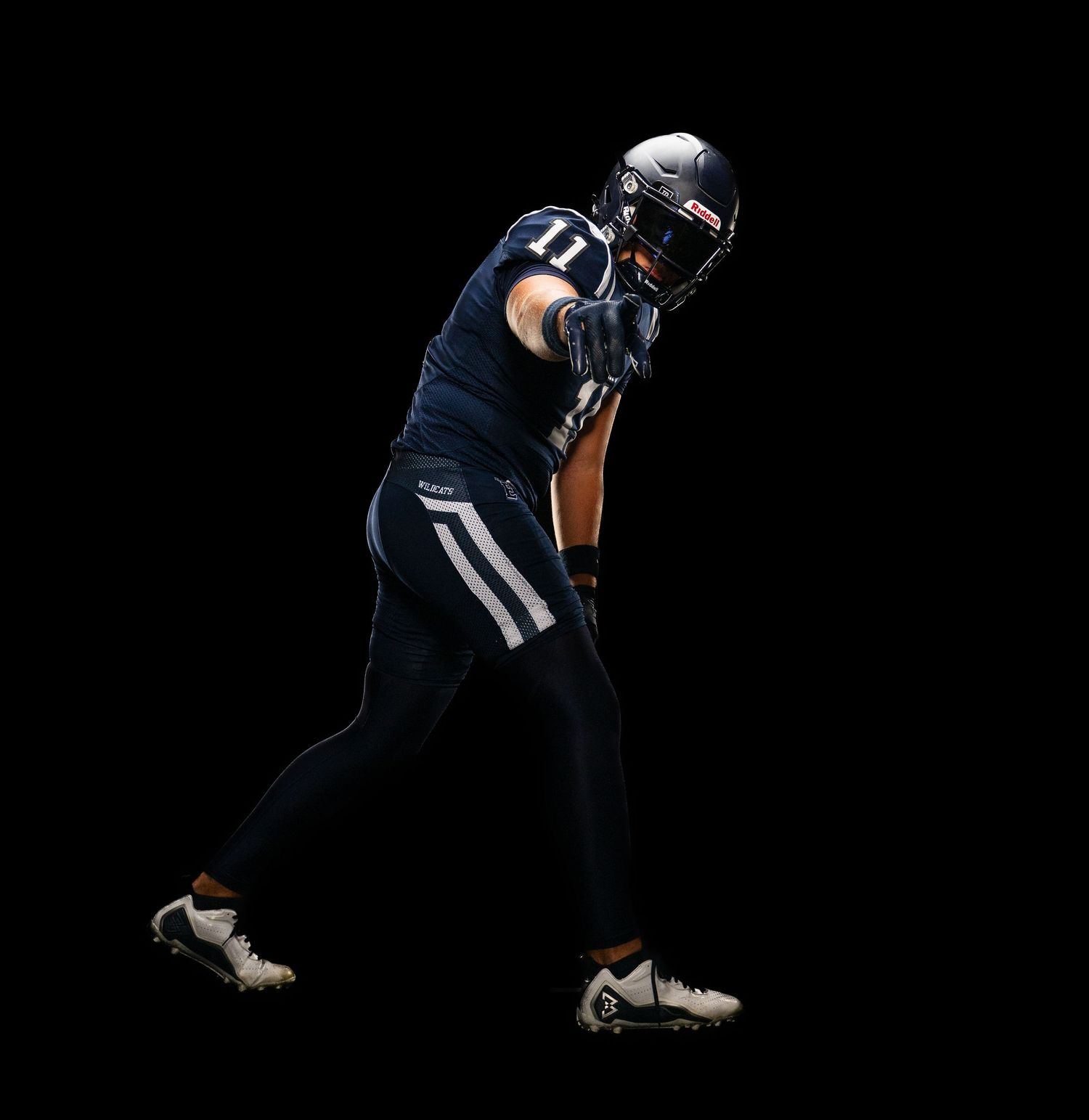 Football player in navy blue uniform and helmet, number 11, posed dynamically against a black background.