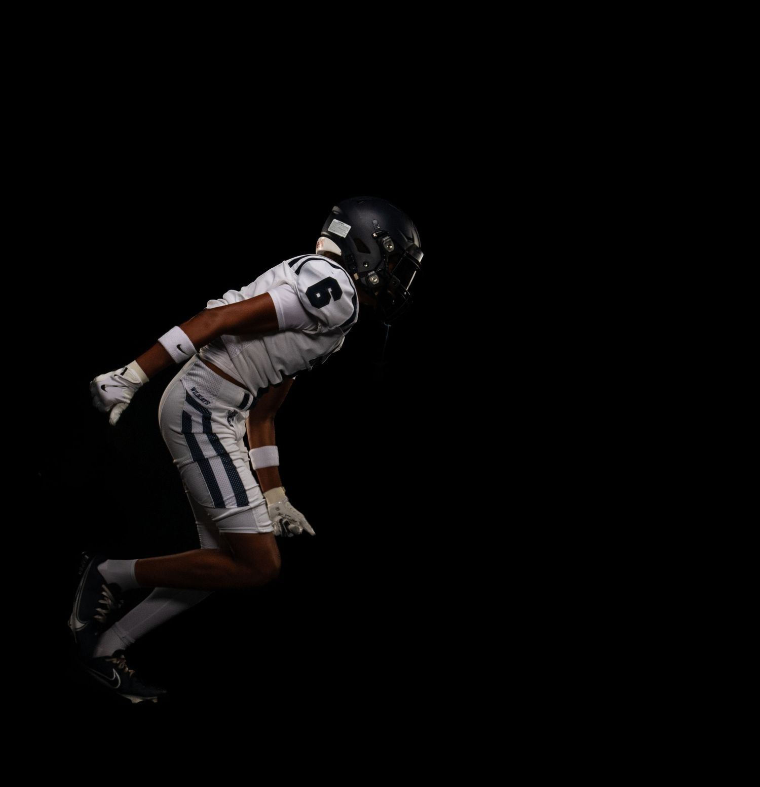 Football player in white uniform sprints in a dynamic pose against a dramatic dark black background.