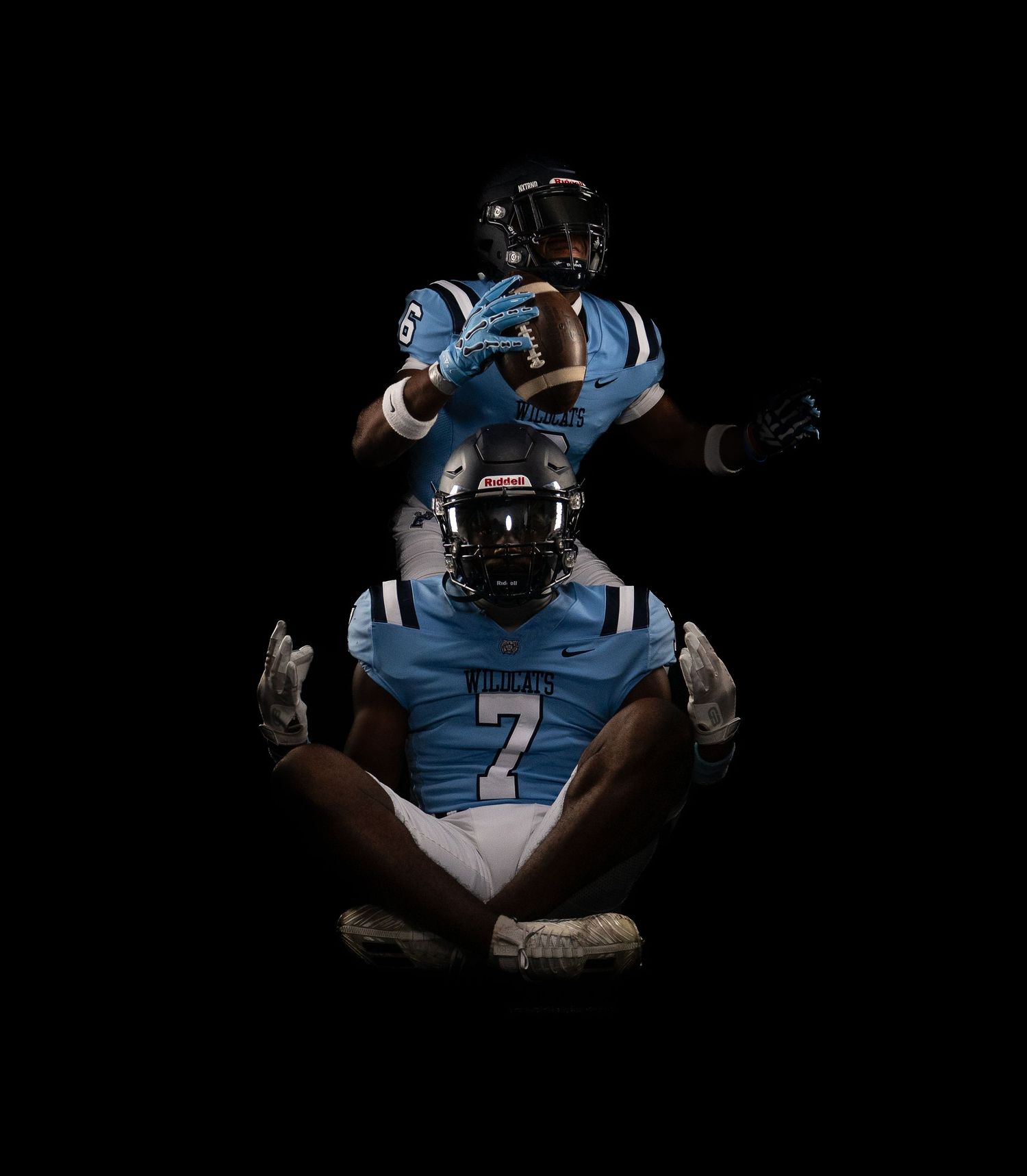 Football player in light blue uniform poses in athletic stance on dark background.
