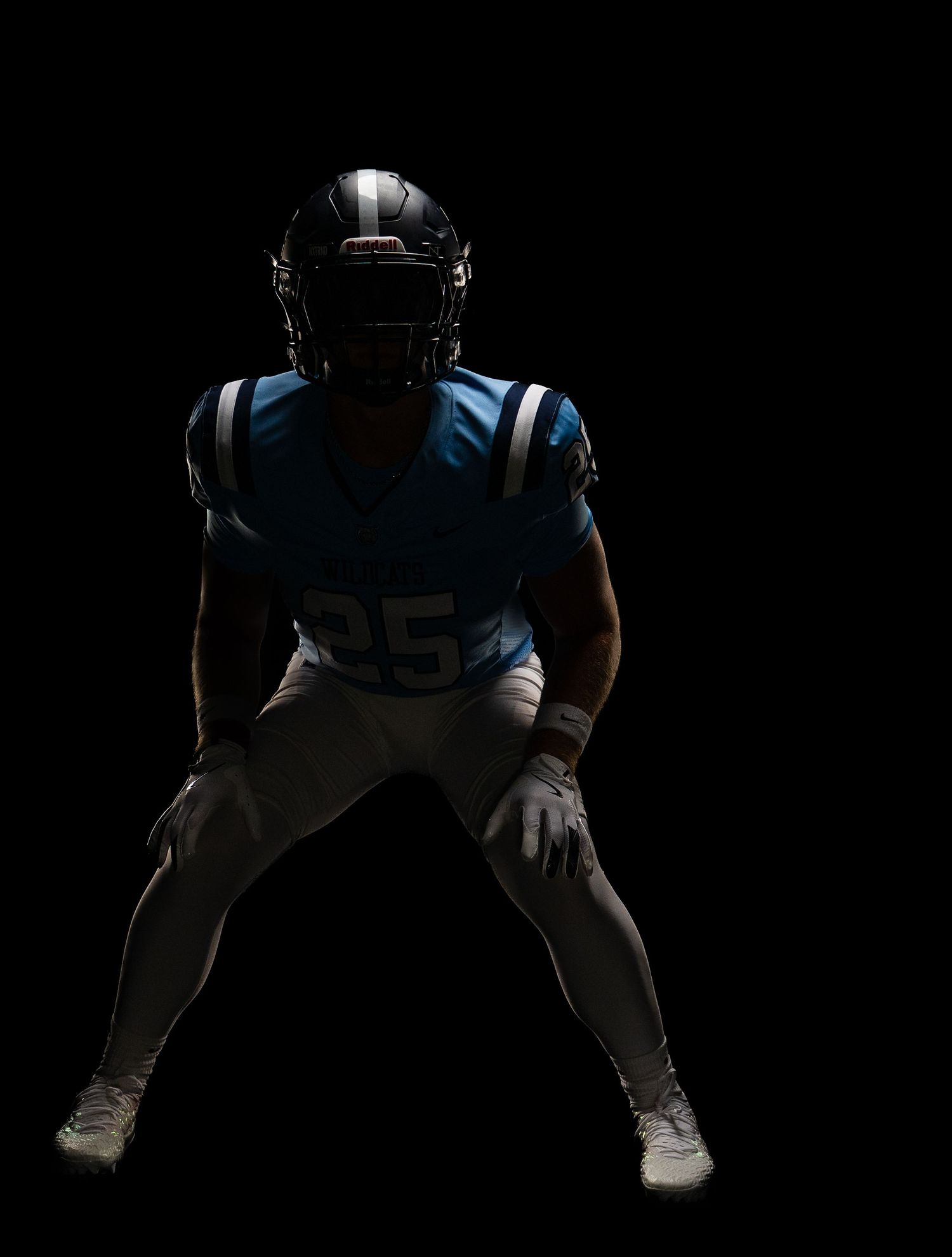 American football player wearing number 25 in blue uniform and helmet posed in athletic stance against black background.