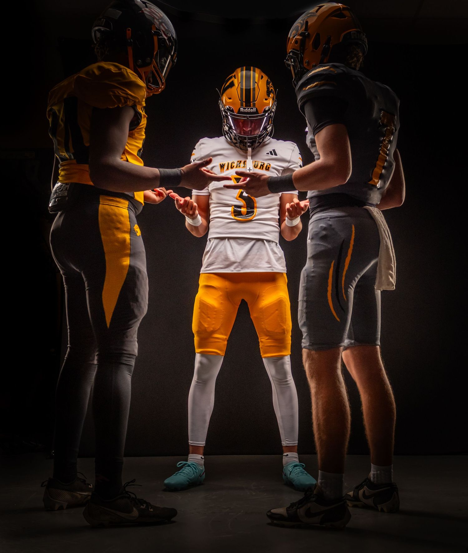 Three football players huddle together in dramatic lighting against dark background.