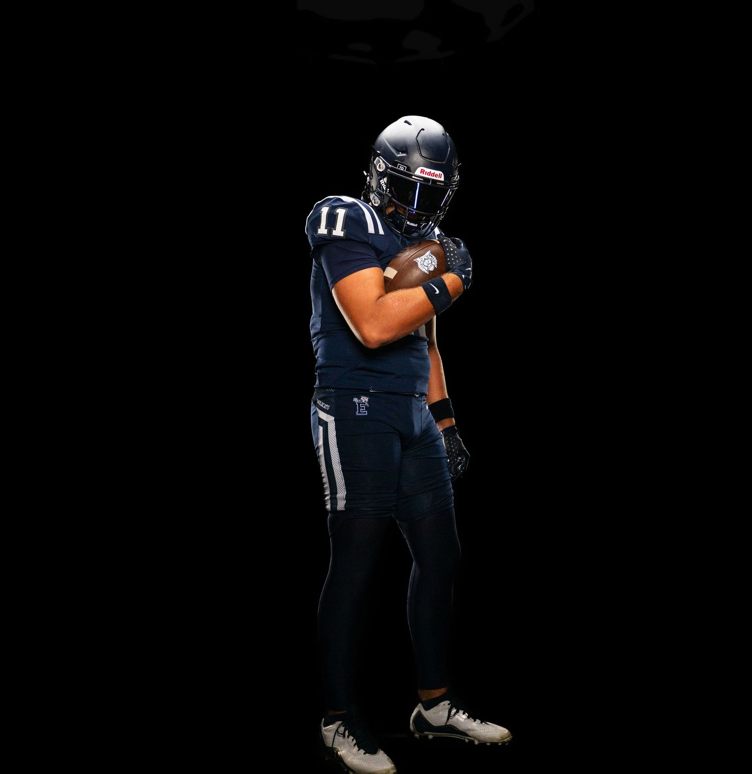 Football player in navy uniform holds ball in dramatic studio lighting.