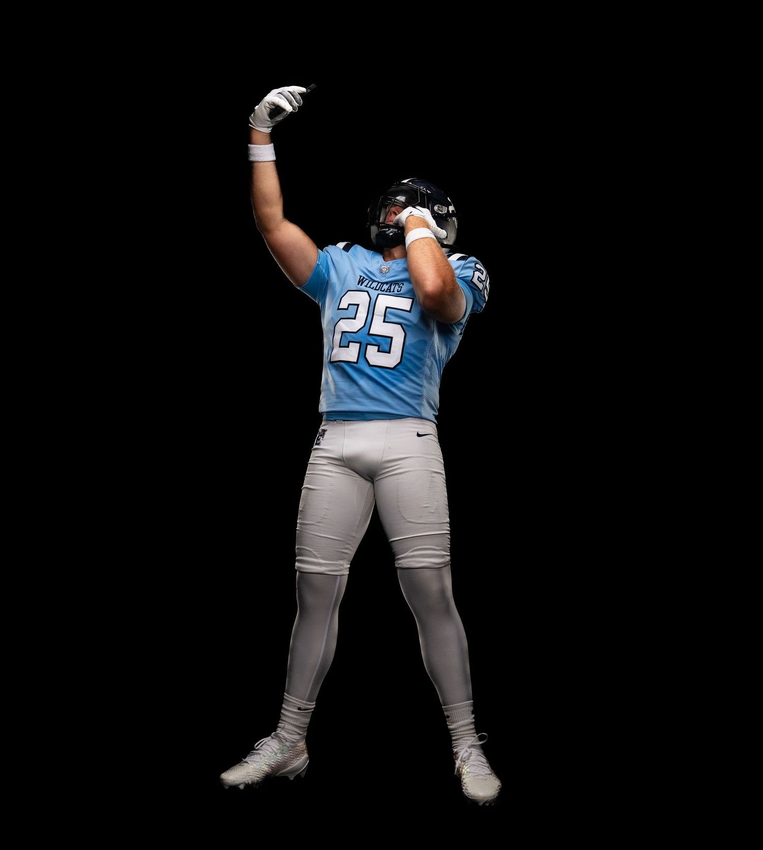 Football player wearing number 25 blue jersey celebrates with raised fist against black background.