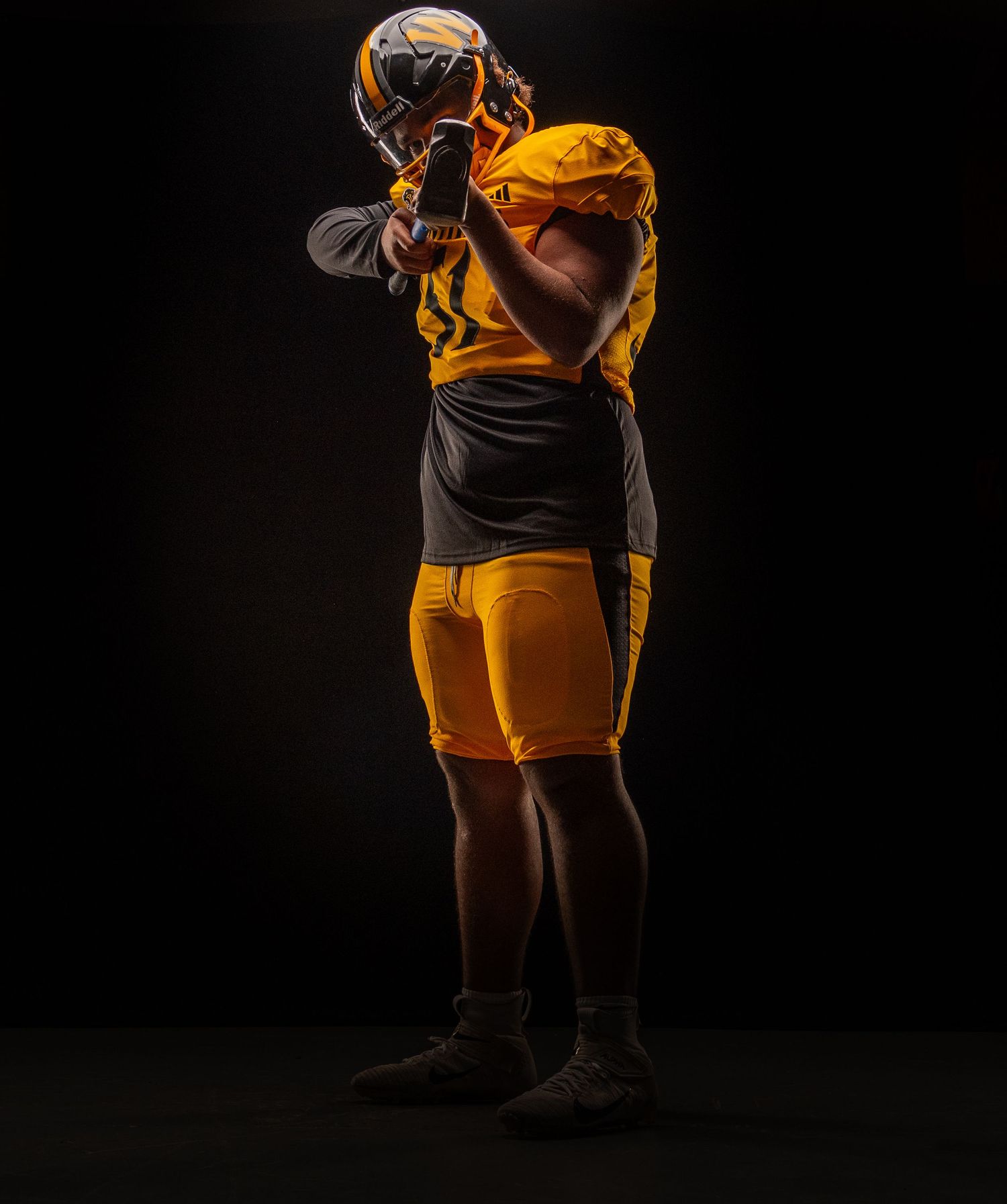 Football player in gold uniform and helmet poses dramatically against a dark background in a professional sports portrait.