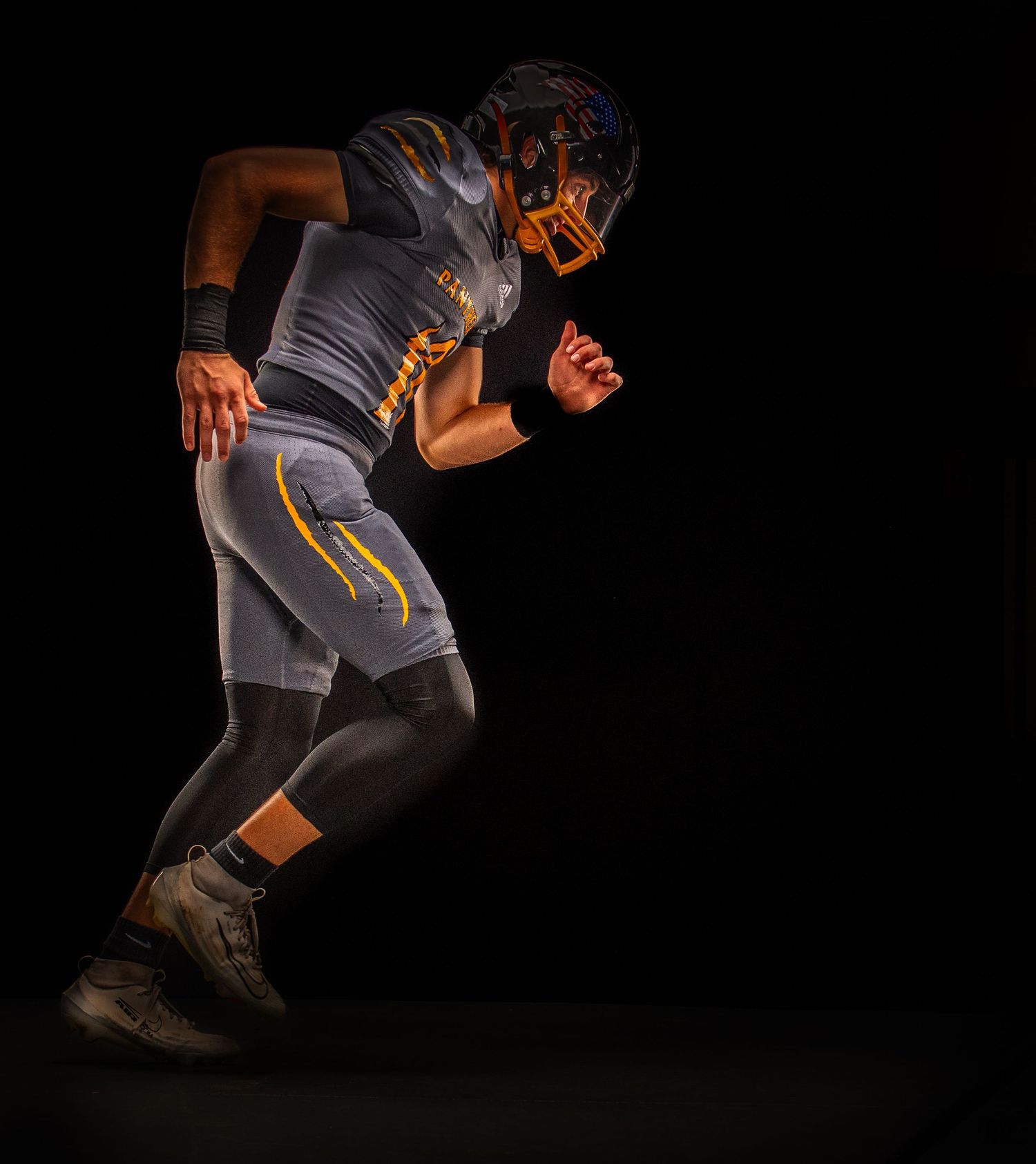 American football player in dark uniform and gold helmet running against a black background.