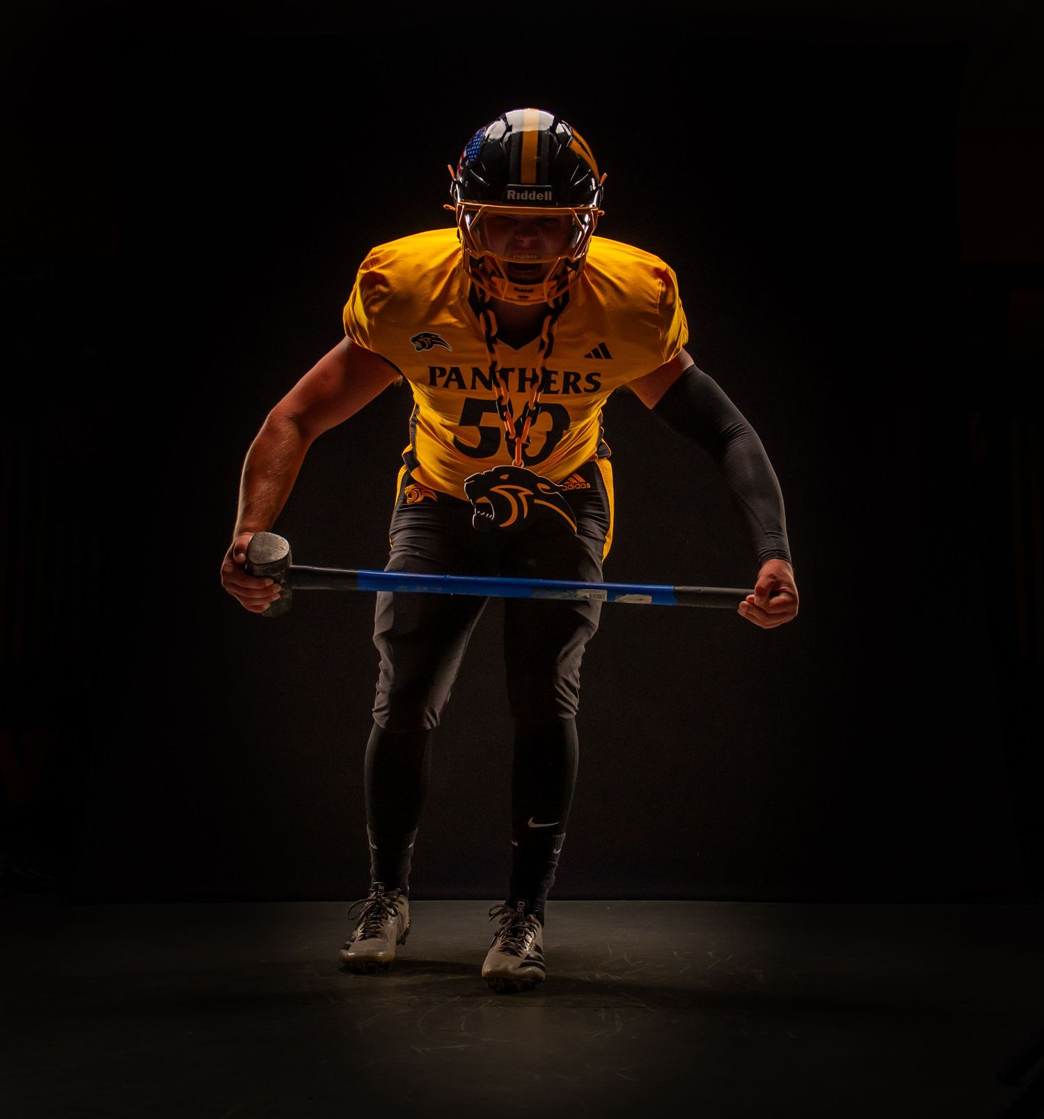 Football player in yellow Panthers jersey number 50 stretches resistance band in dramatic studio lighting.