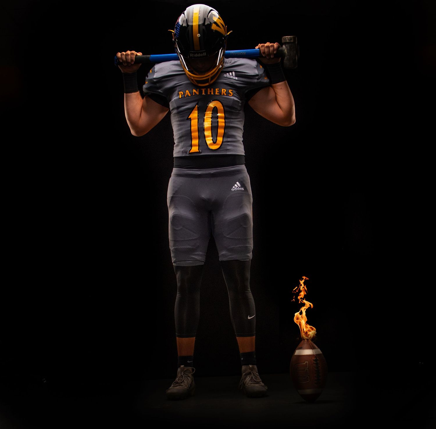 Football player in orange jersey and gray pants photographed against black background.