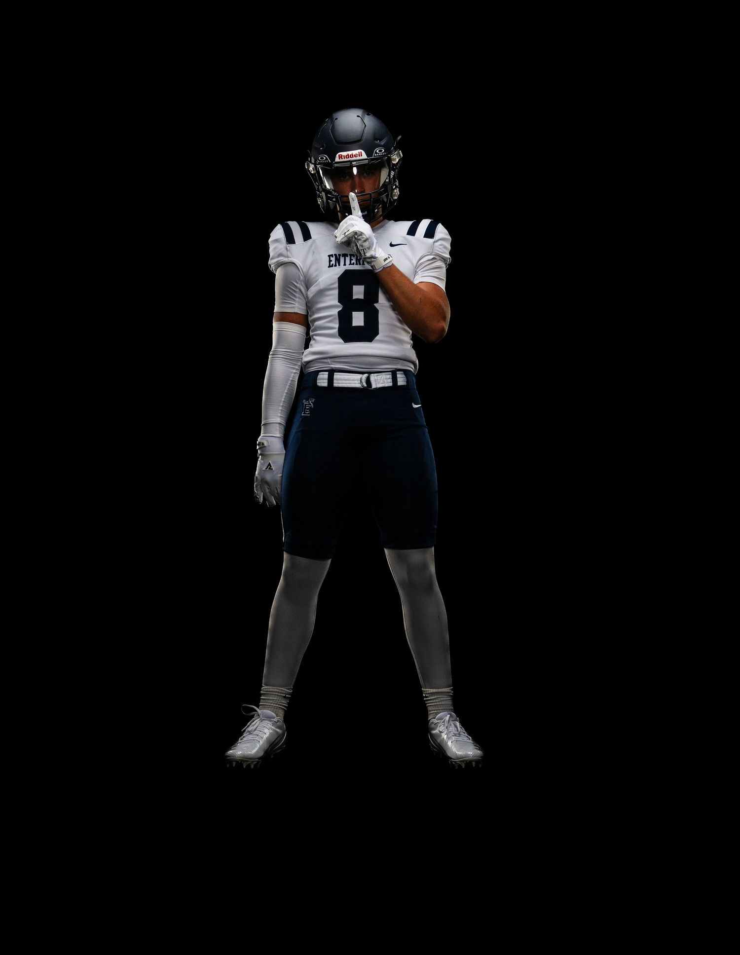 Football player number 8 in white and navy uniform stands confidently on dark background.