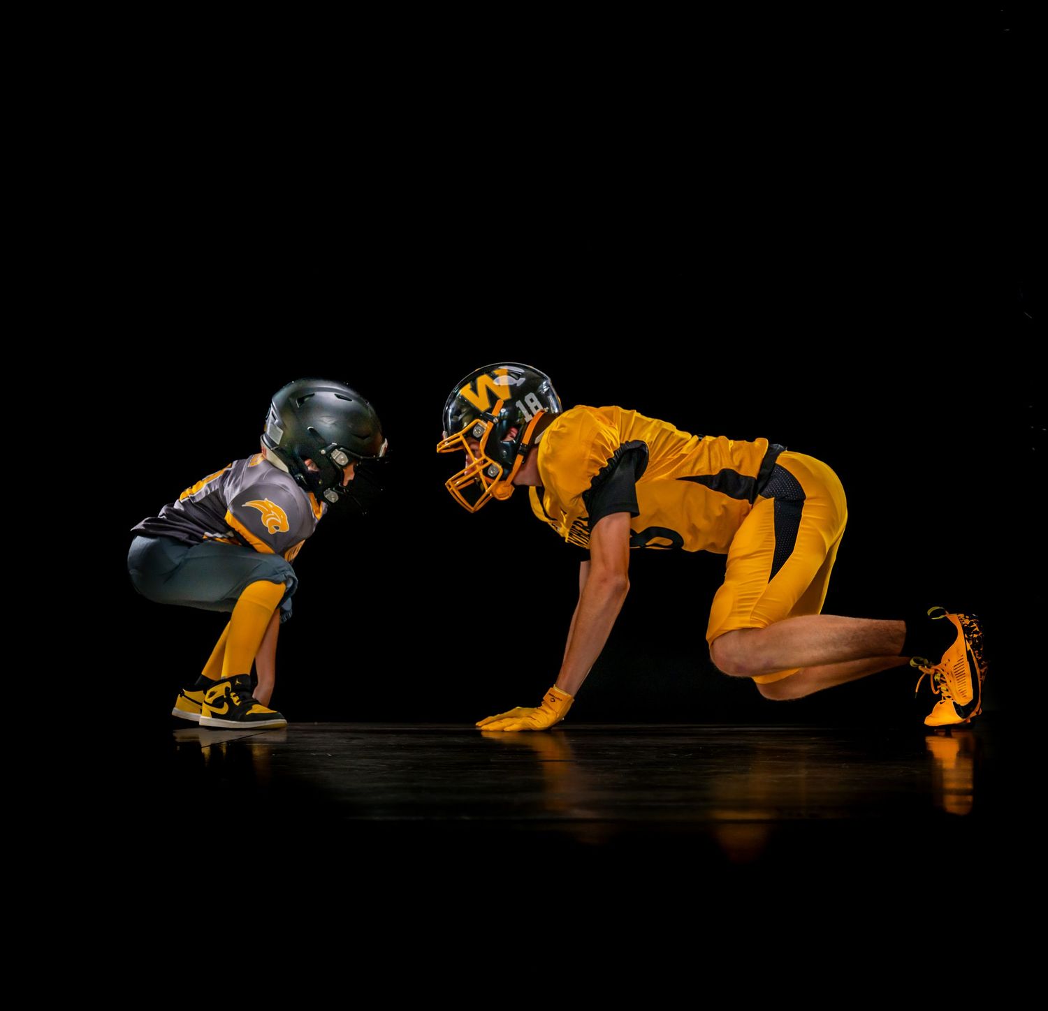 Two football players in gold and dark uniforms facing off in scrimmage stance.