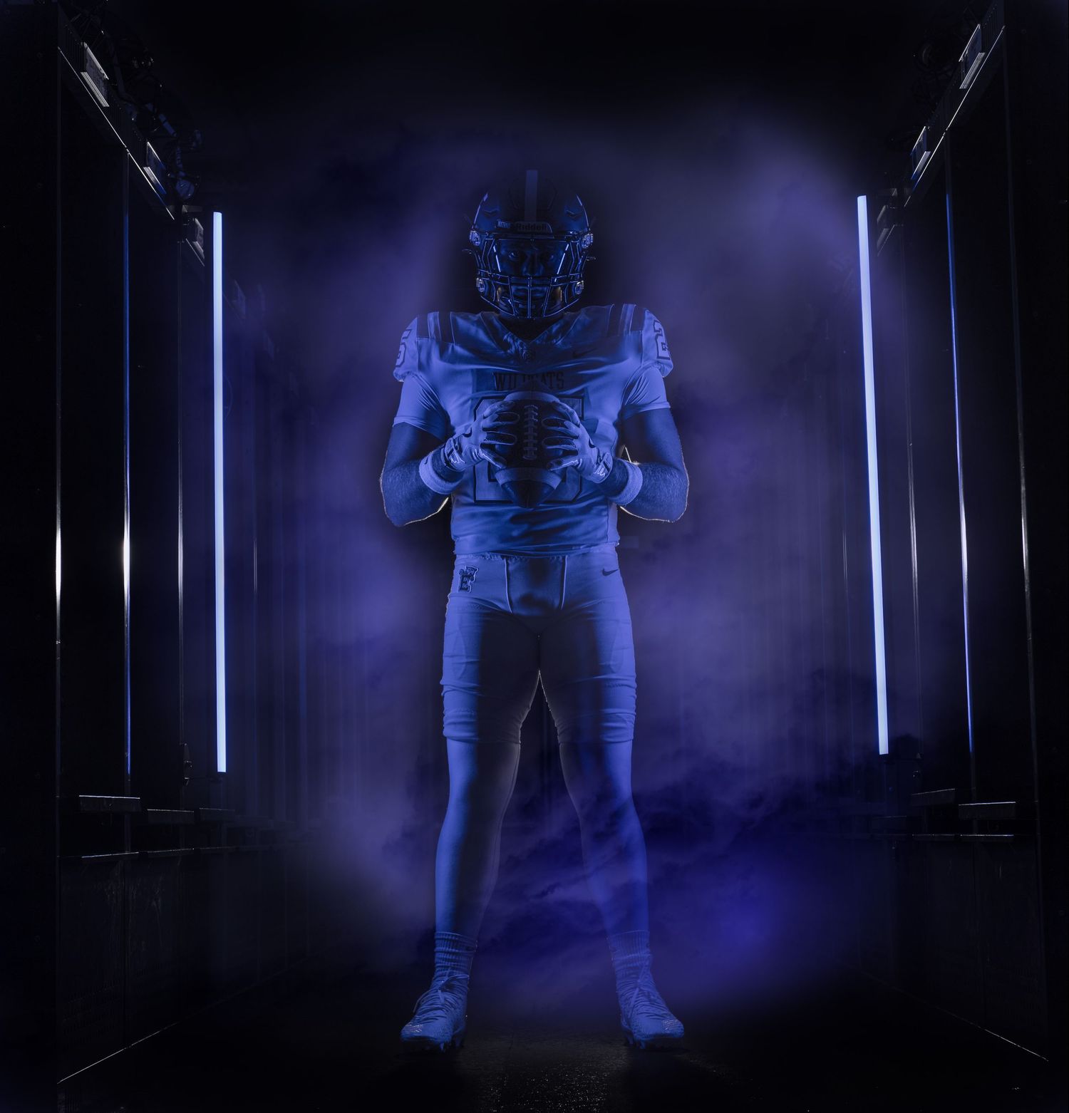 Football player in blue uniform poses dramatically in dark tunnel with glowing neon lights and purple smoke.