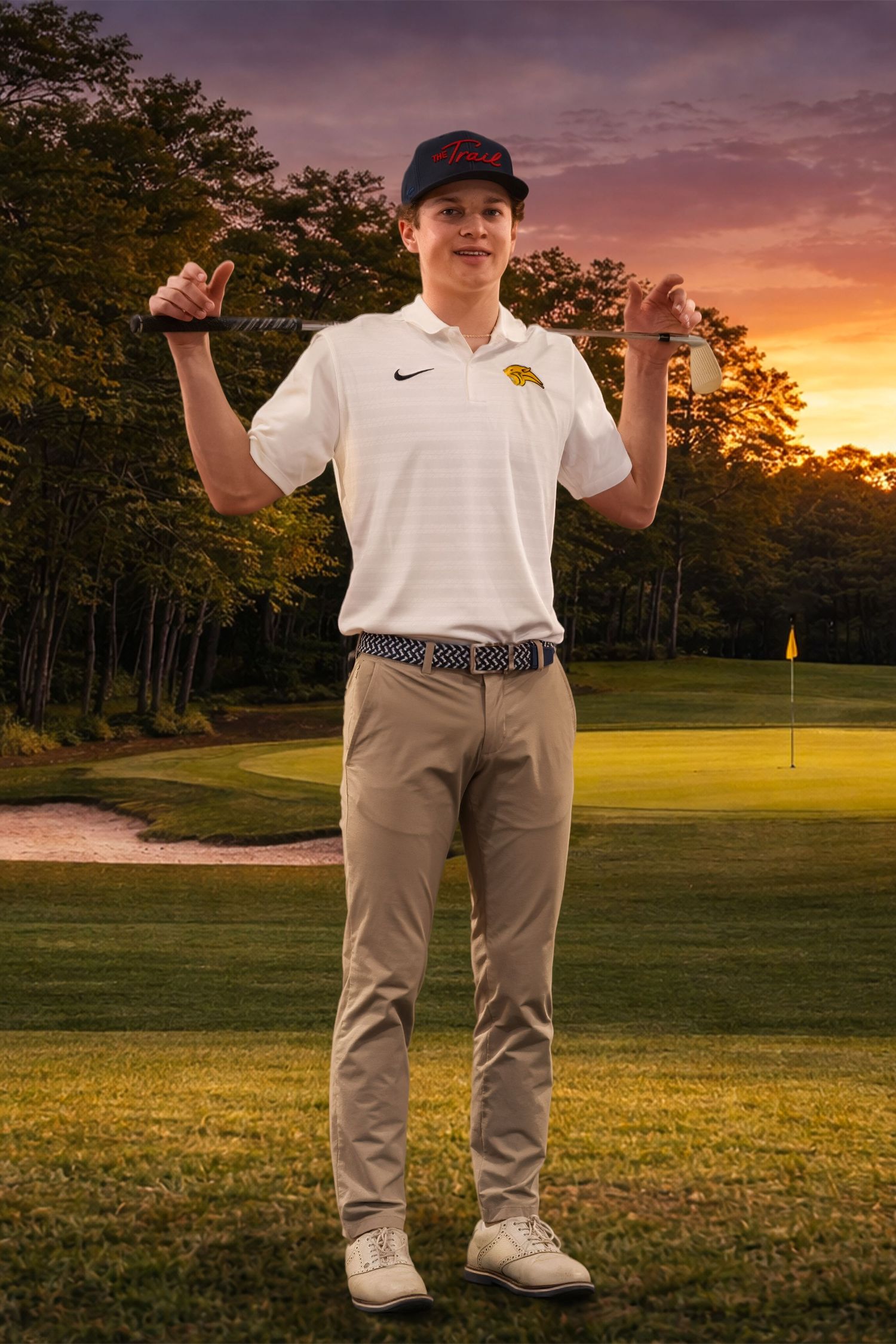 Golfer in white polo and khaki pants poses on golf course during dramatic sunset with trees in background.