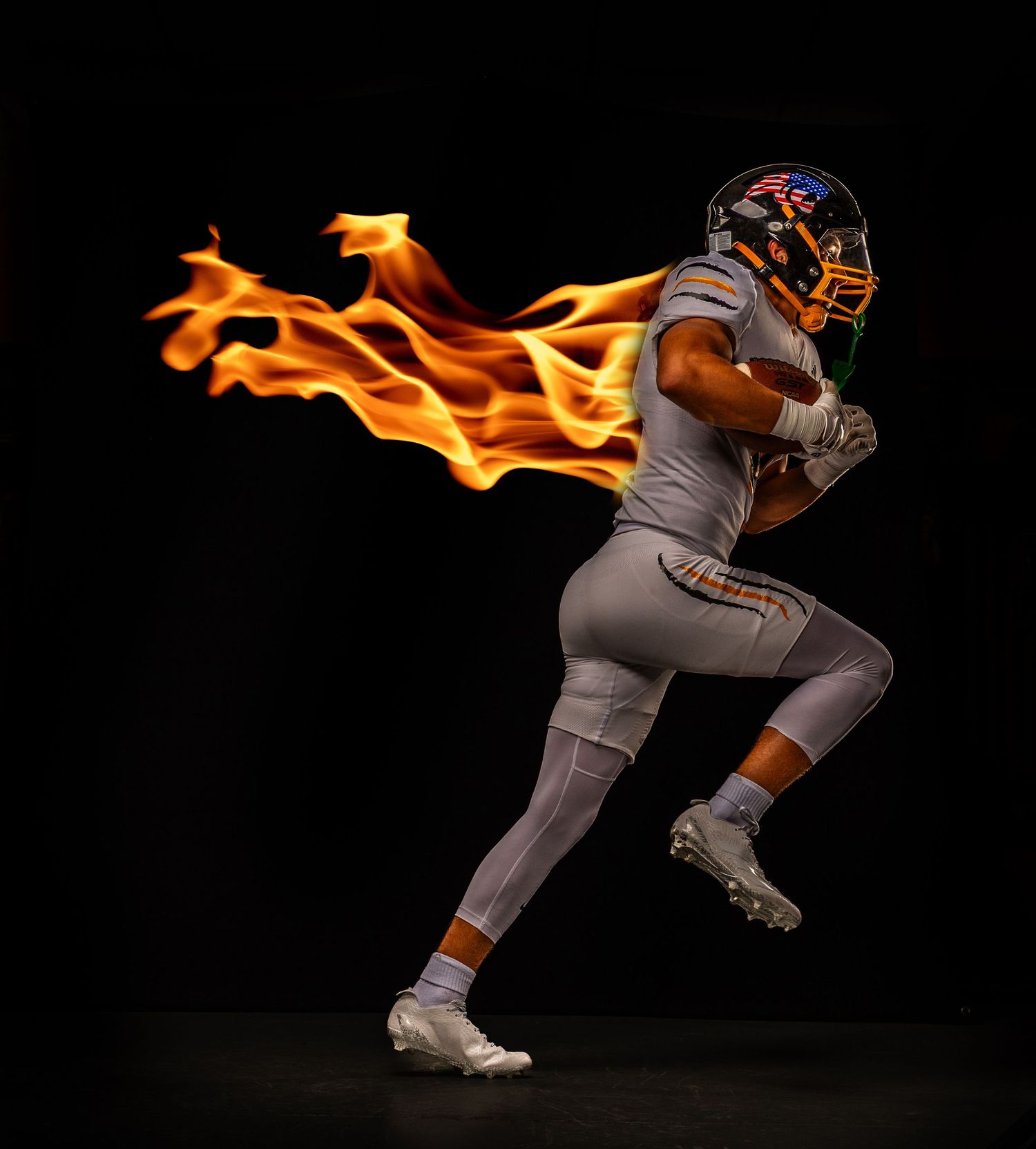 Football player in white uniform running with dramatic fire effect against black background.