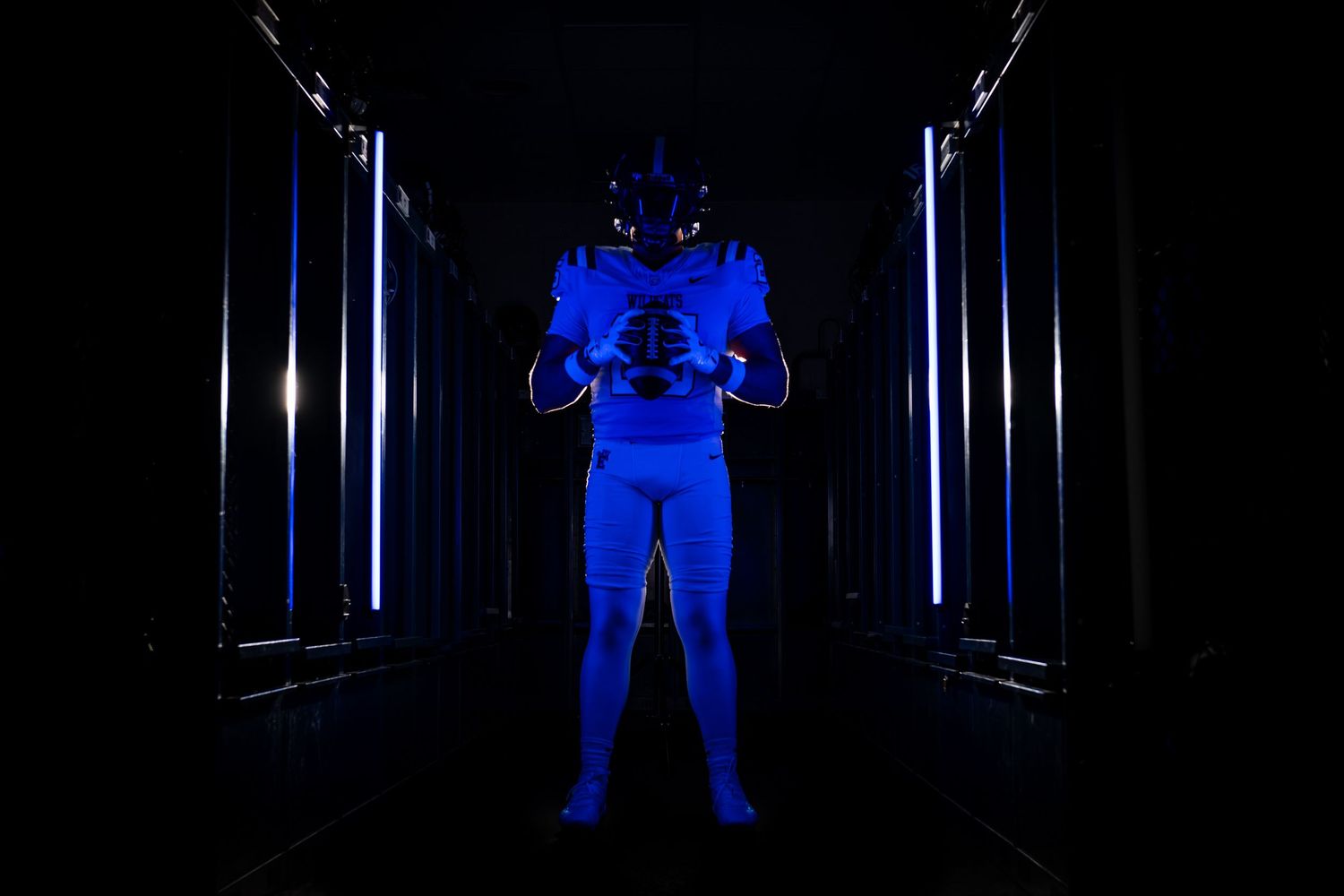 Football player in all-blue uniform poses in a dark tunnel with dramatic blue lighting on both sides.