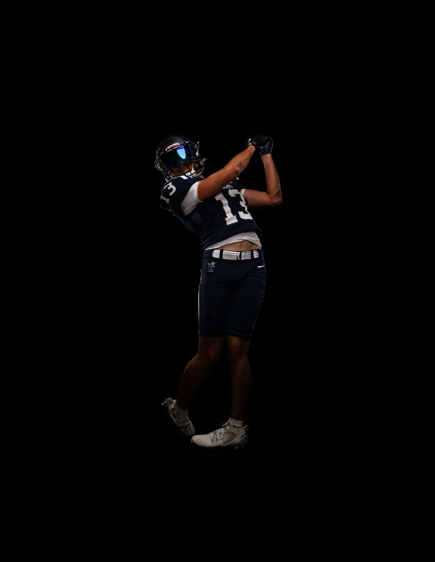 Football player #13 in dark blue uniform swinging in a golf pose against black background.