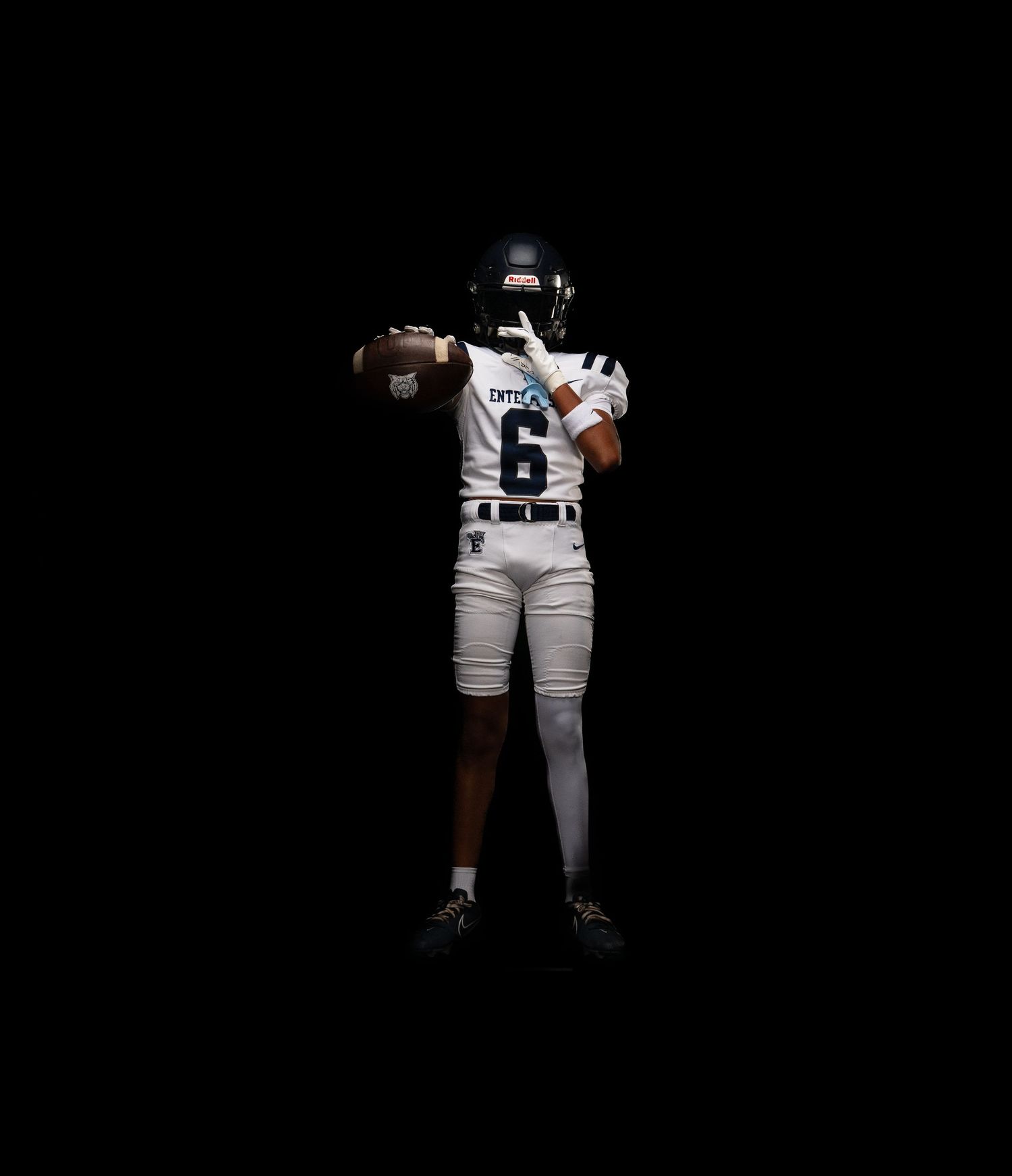 Football player in white jersey number 6 prepares to throw ball against dark background.
