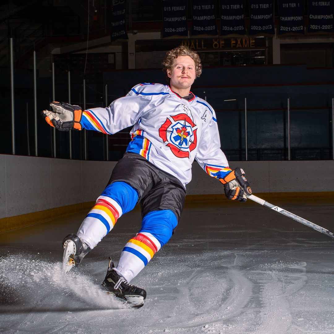 BCIHL Okanagan Lakers player dramatically skates past in a dark arena.