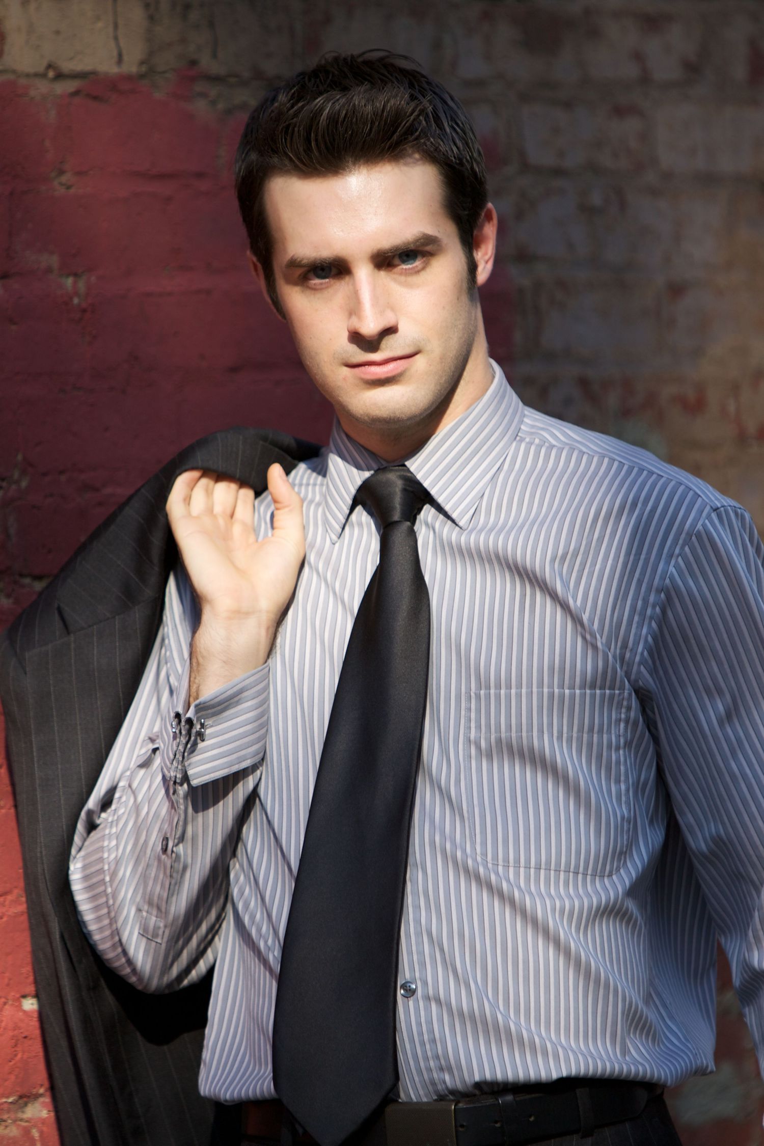 Professional headshots against a brick wall featuring someone in a striped dress shirt and dark tie.