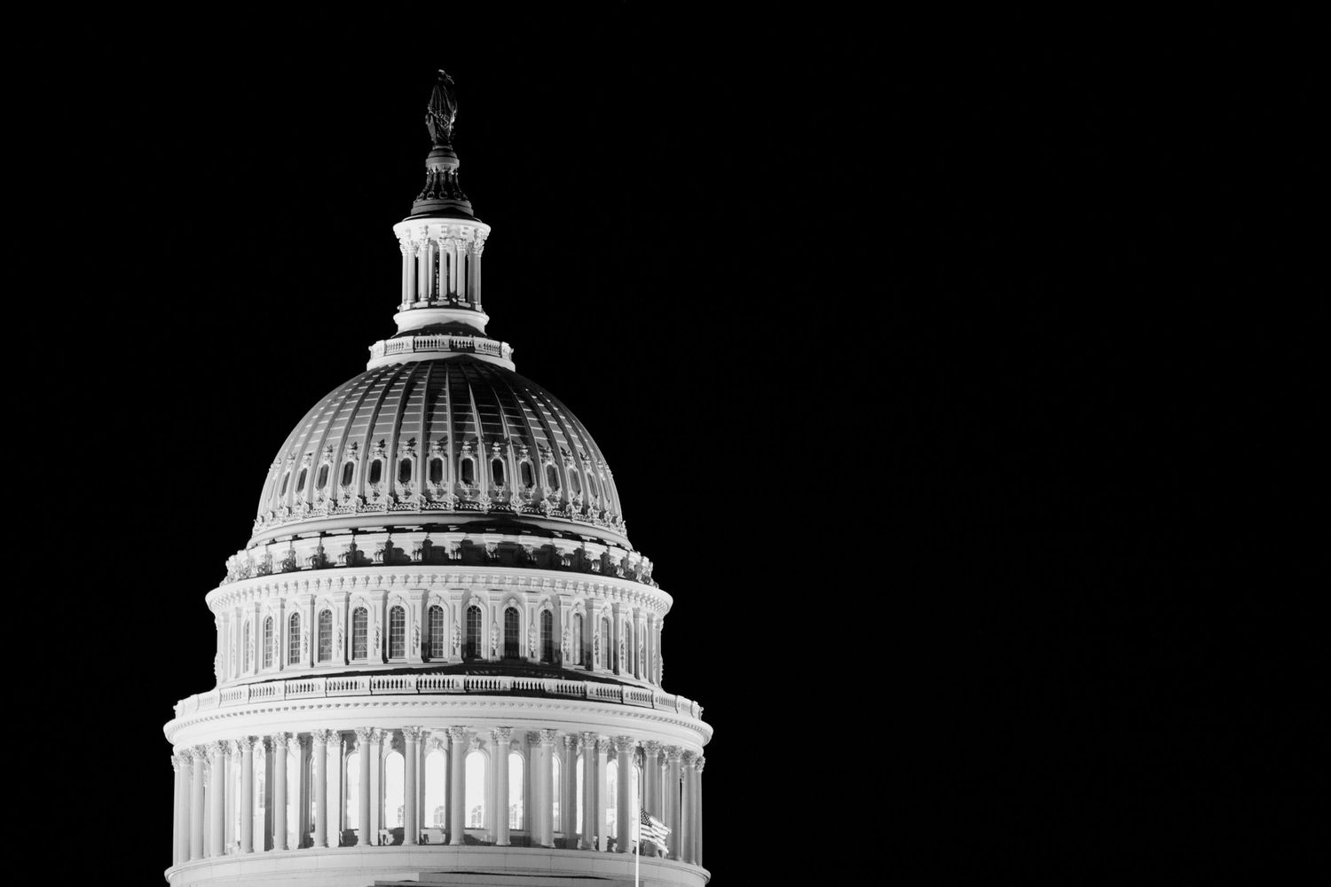 Black and white architectural detail of the US Capitol Building dome against a dark sky.