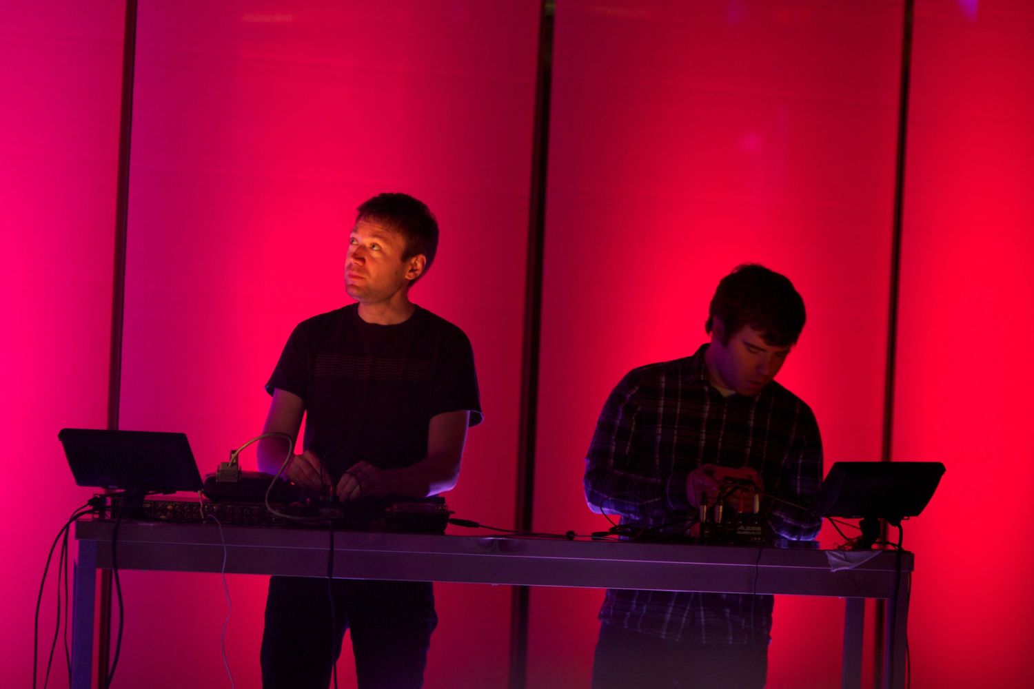 Musicians performing on stage with red lighting and electronic equipment.