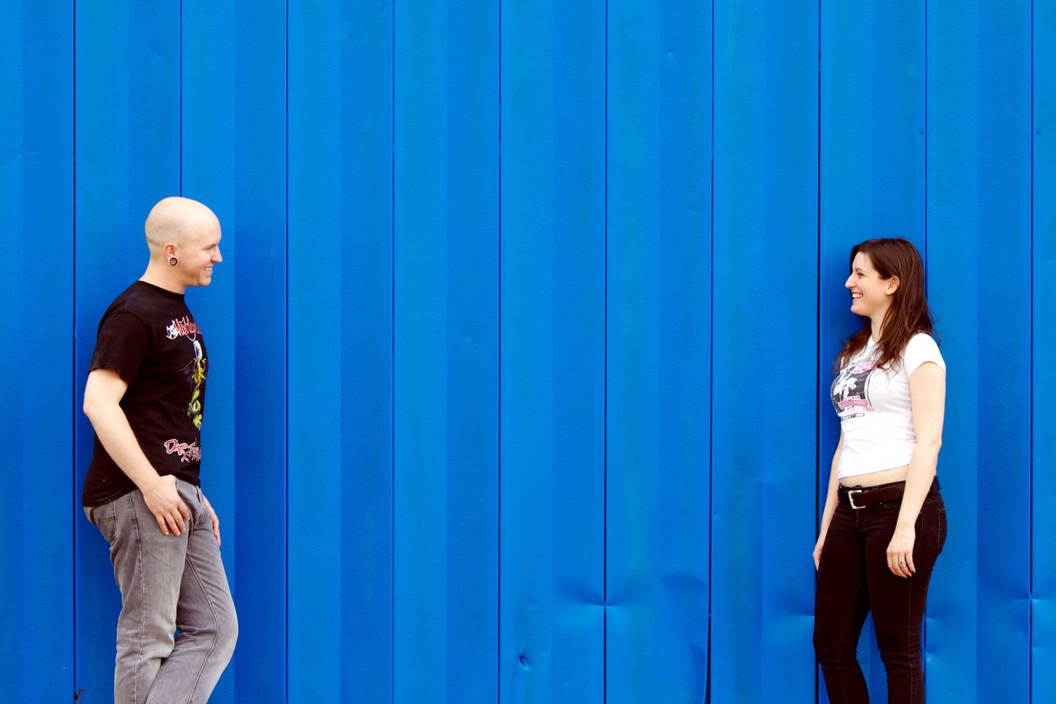 Two people standing against bright blue wall in casual conversation.