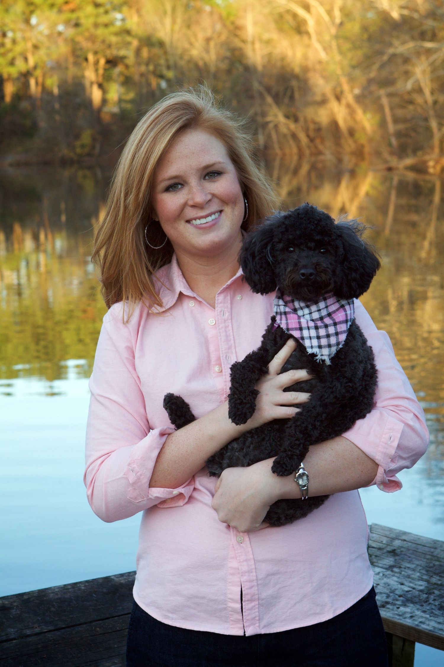 Outdoor portrait with small black poodle puppy by lake in autumn.