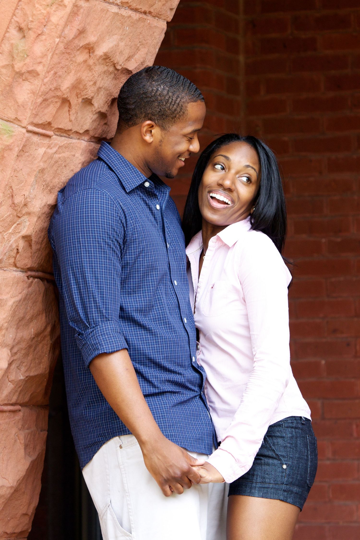 A romantic couple shares tender moments against a brick wall wearing blue and pink shirts.