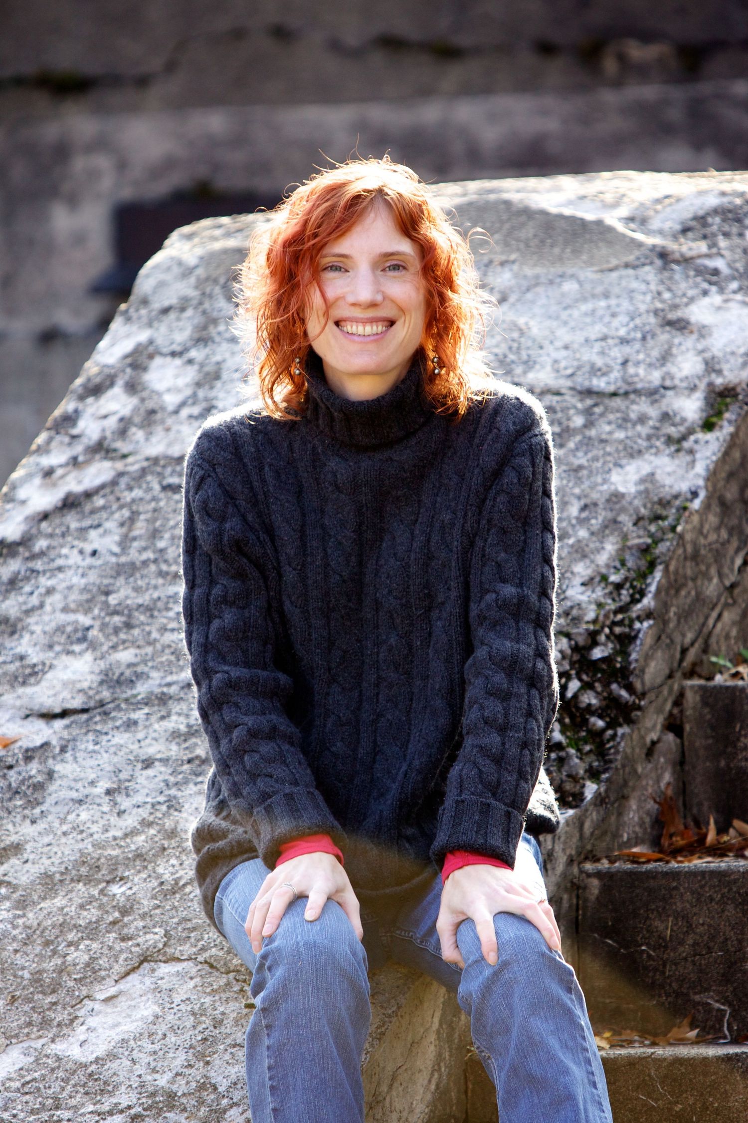 Person wearing navy cable knit sweater sitting casually on large rock formation outdoors.