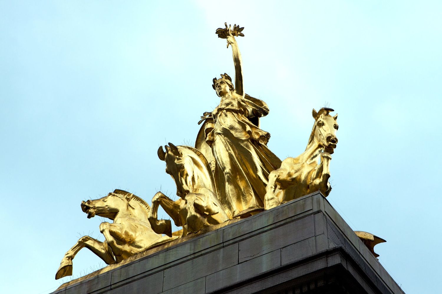 Golden sculptural figures adorning the top of a classical building against a blue sky.