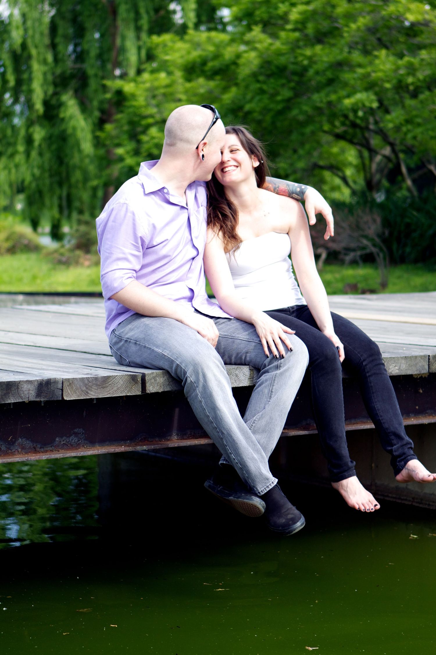Couple sharing intimate moment while sitting on wooden dock by pond.