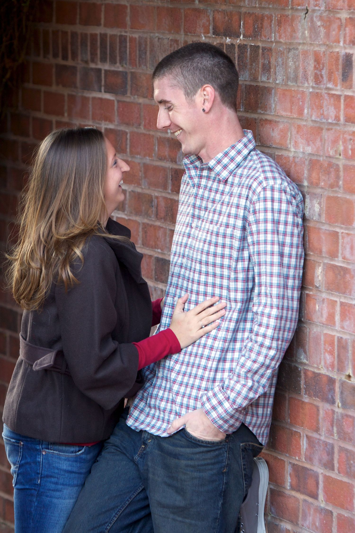 Casual couple poses against rustic brick wall background.
