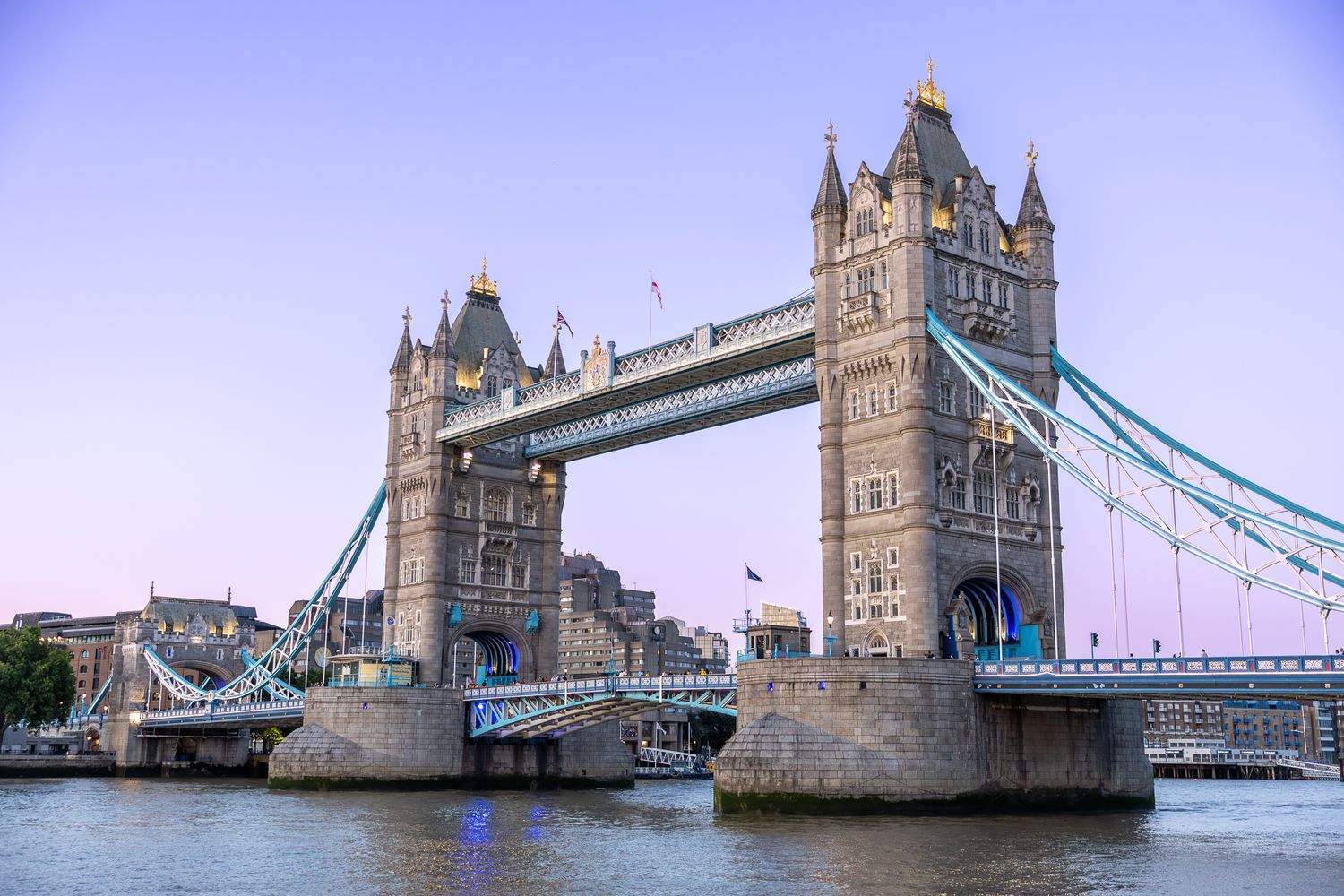 London's Tower Bridge spans the River Thames at dusk with purple sky.