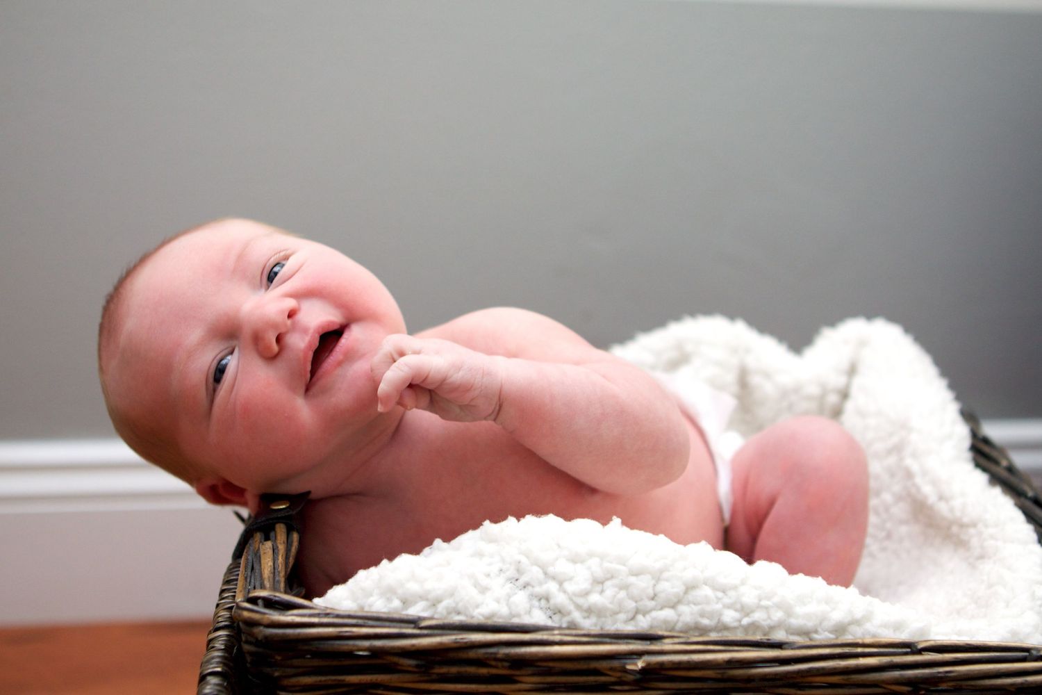 Newborn baby lying on soft white blanket smiling.