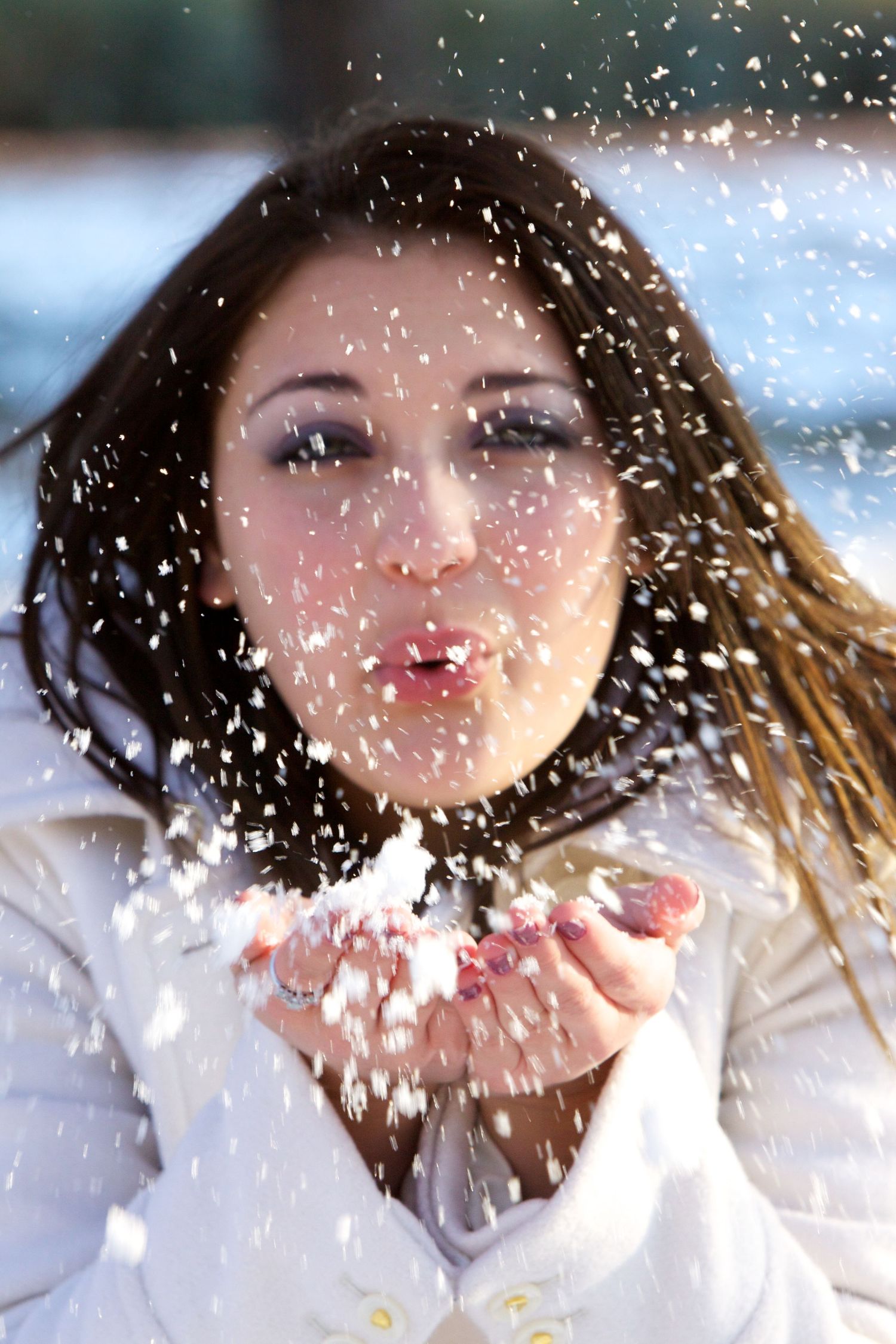 Person in white coat blowing snow in winter scene.