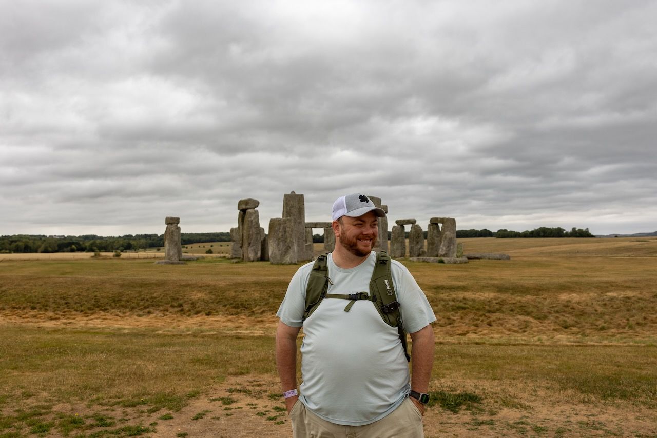 A tourist poses in front of the ancient Stonehenge monument on an overcast day.